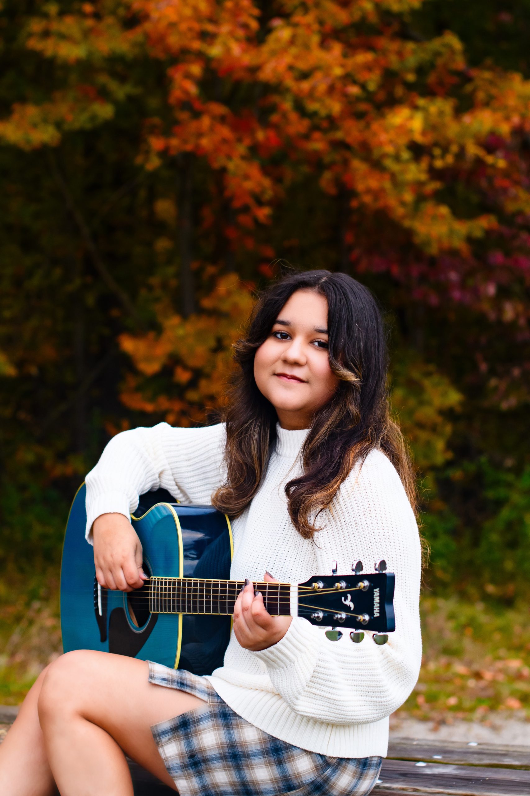 Carmen seated on a bench with guitar during Allen Park 2025 senior photography session