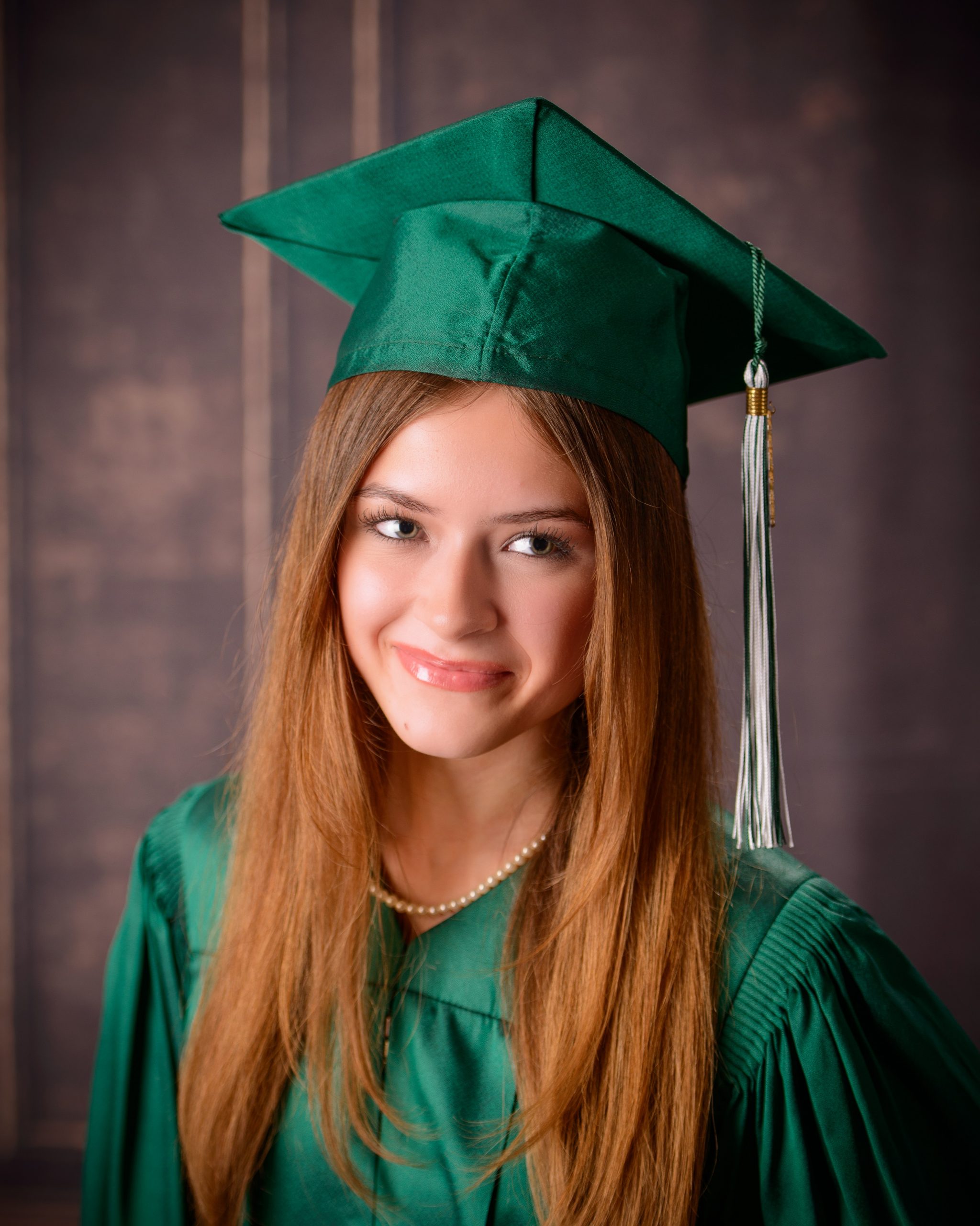 Senior photo session featuring green graduation cap and gown, holding cap in mansion studio setting