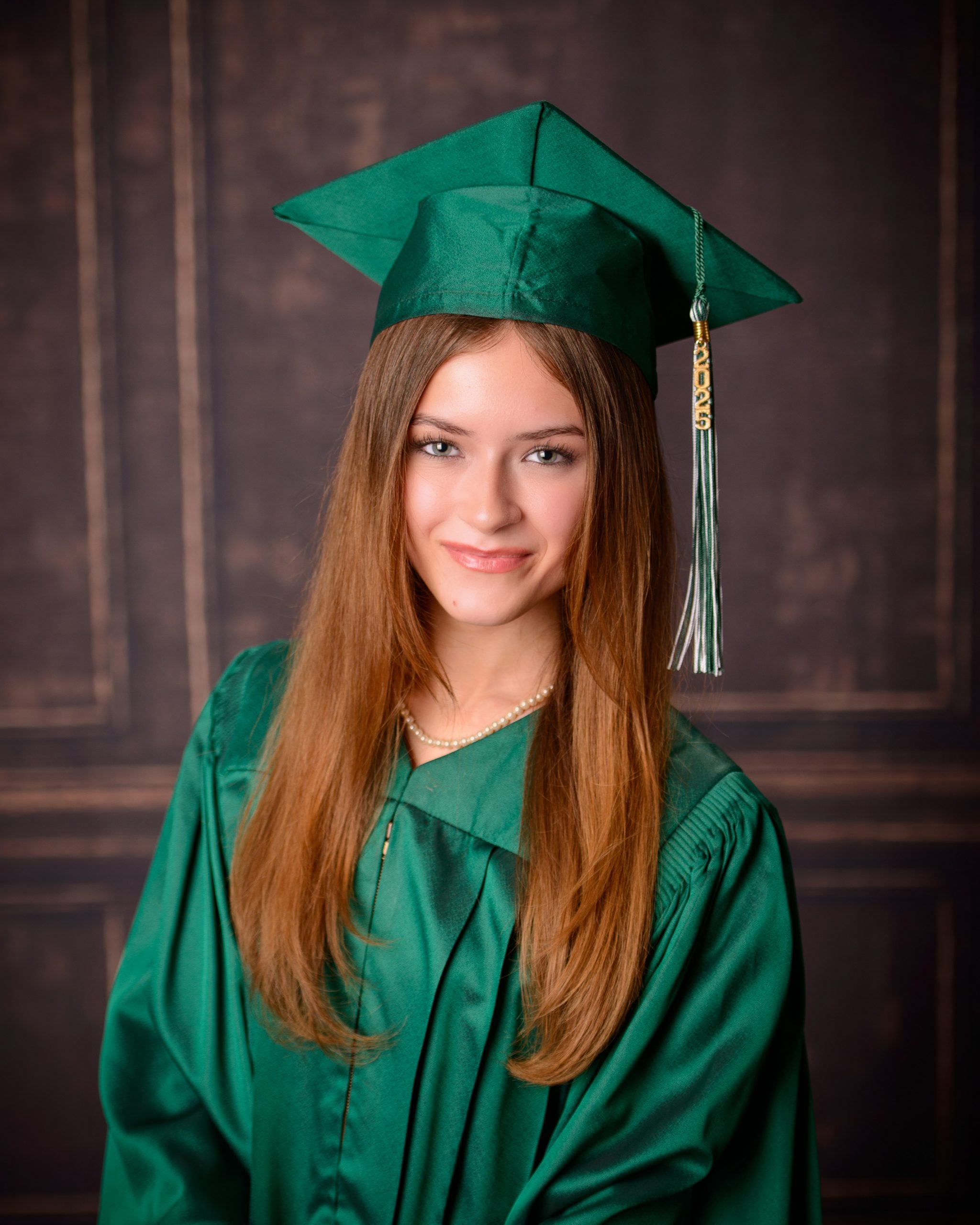 Senior photo session featuring green graduation cap and gown, holding cap in mansion studio setting