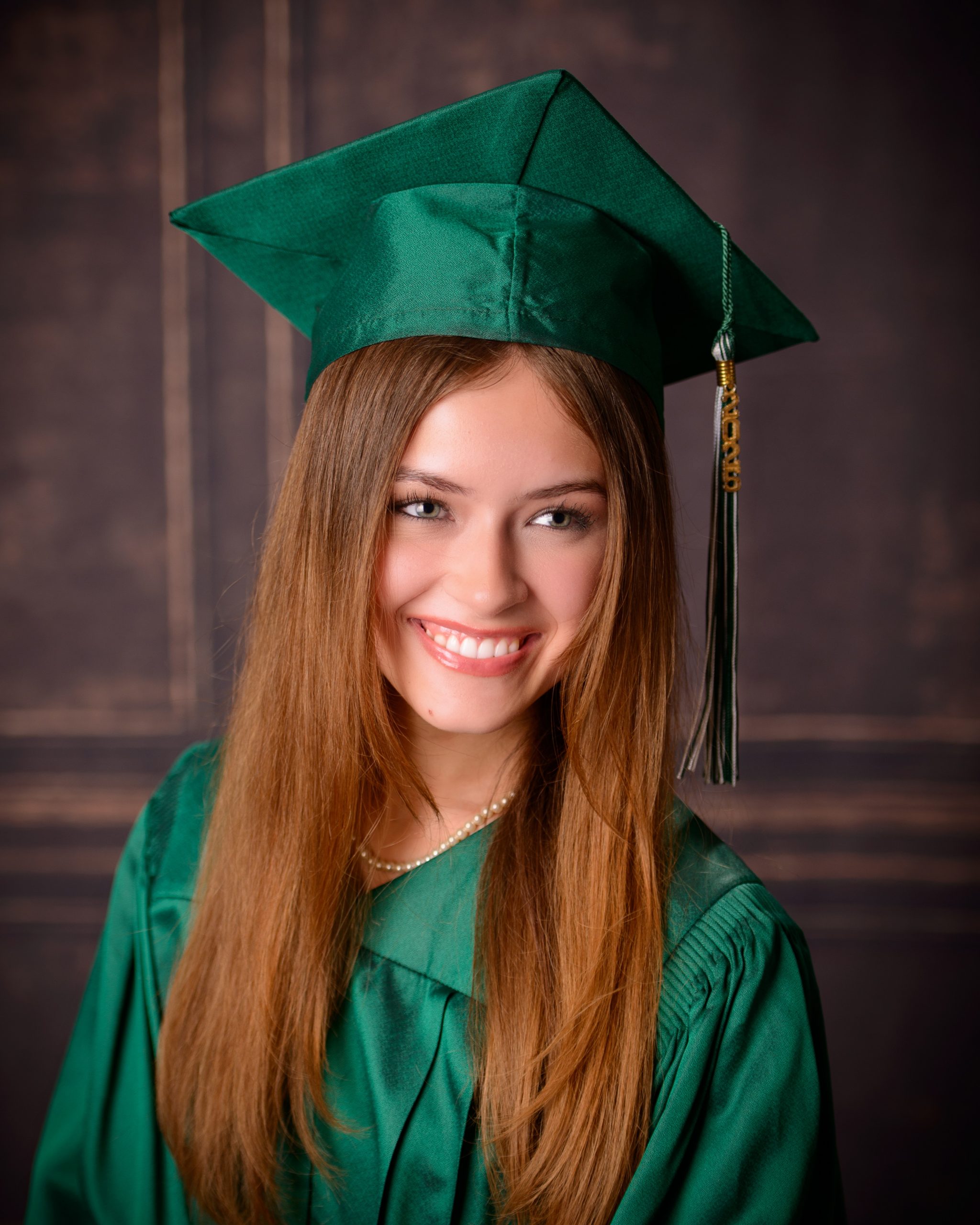Senior photo session featuring green graduation cap and gown, holding cap in mansion studio setting