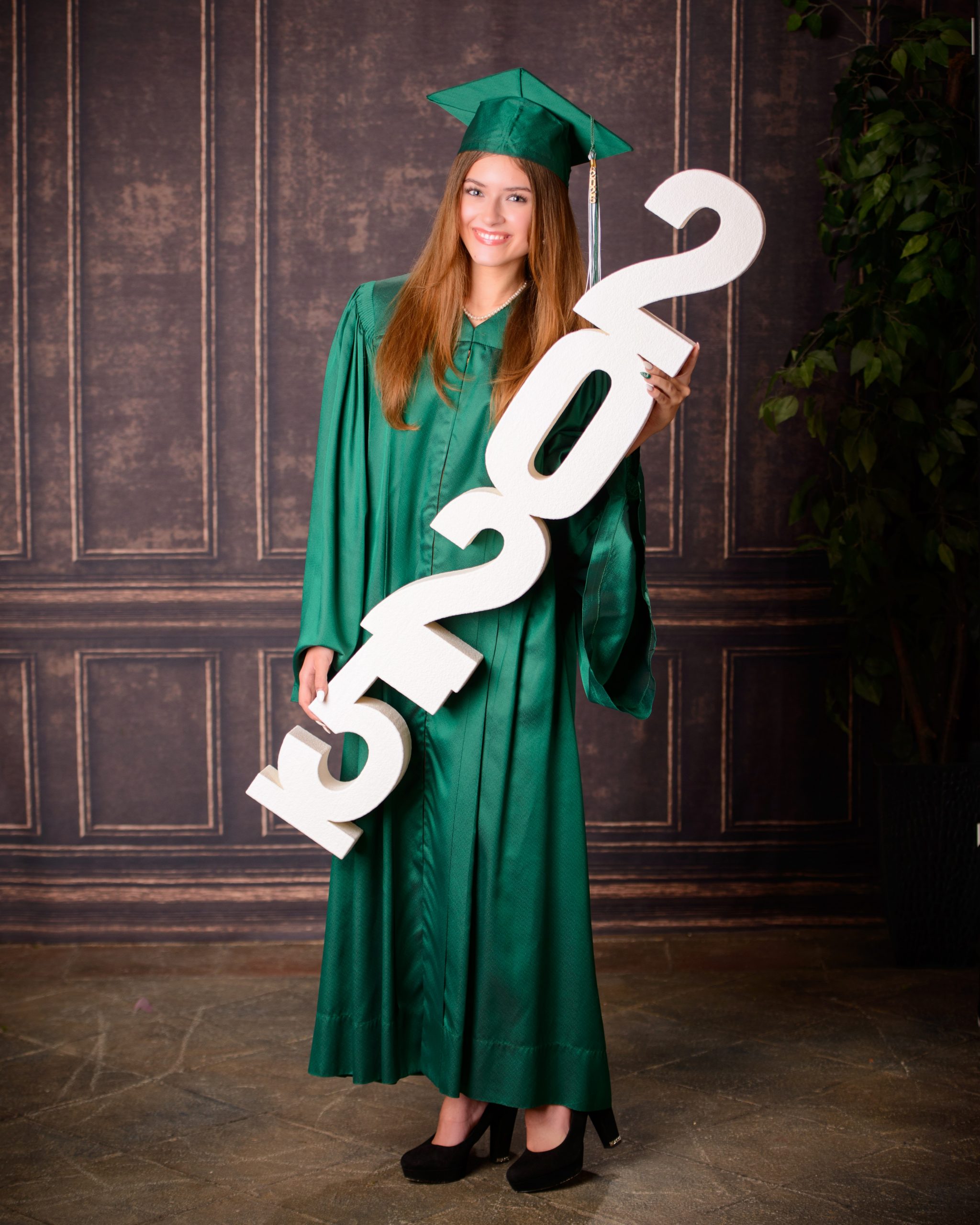Senior photo session featuring green graduation cap and gown, holding cap in mansion studio setting