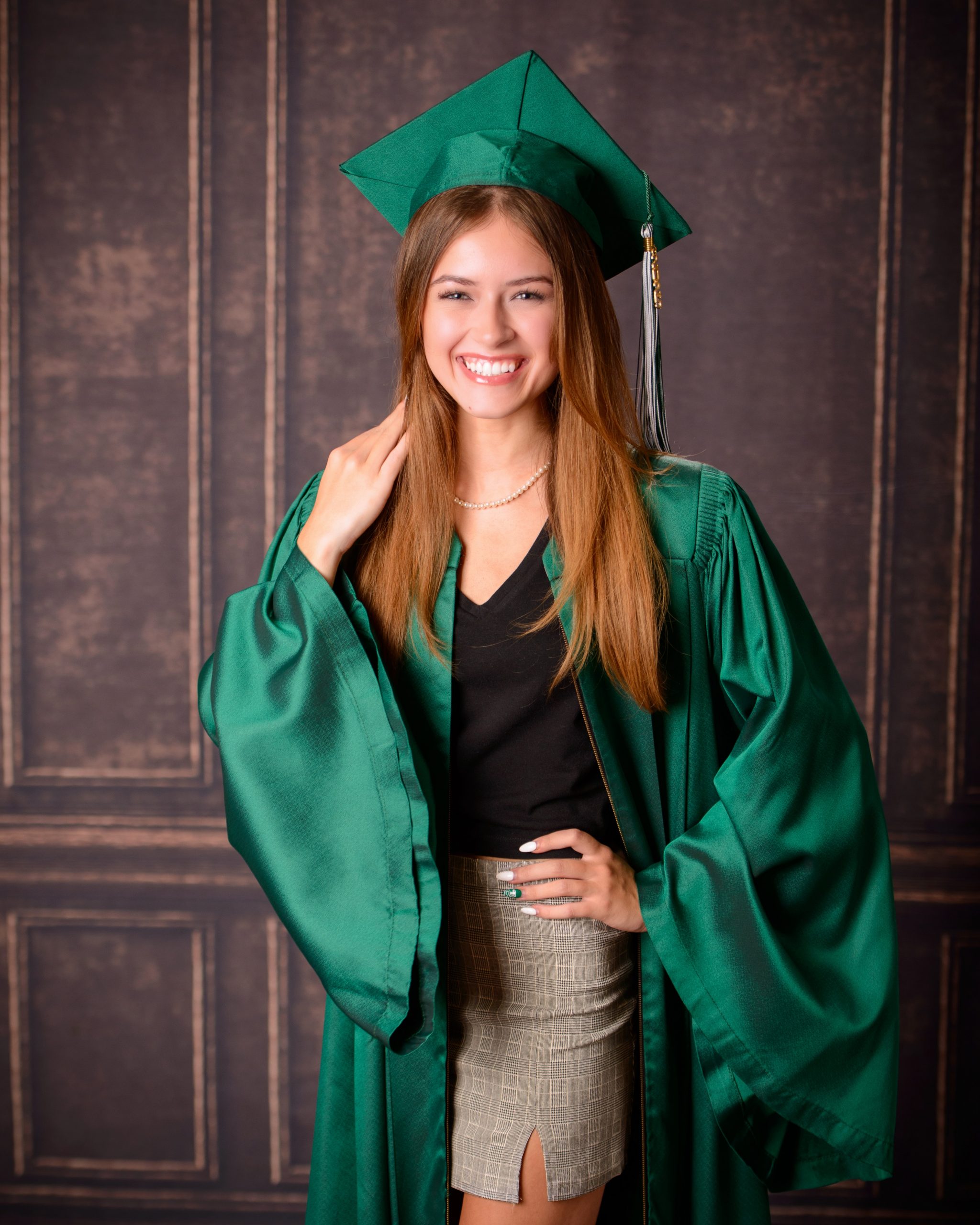 Senior photo session featuring green graduation cap and gown, holding cap in mansion studio setting