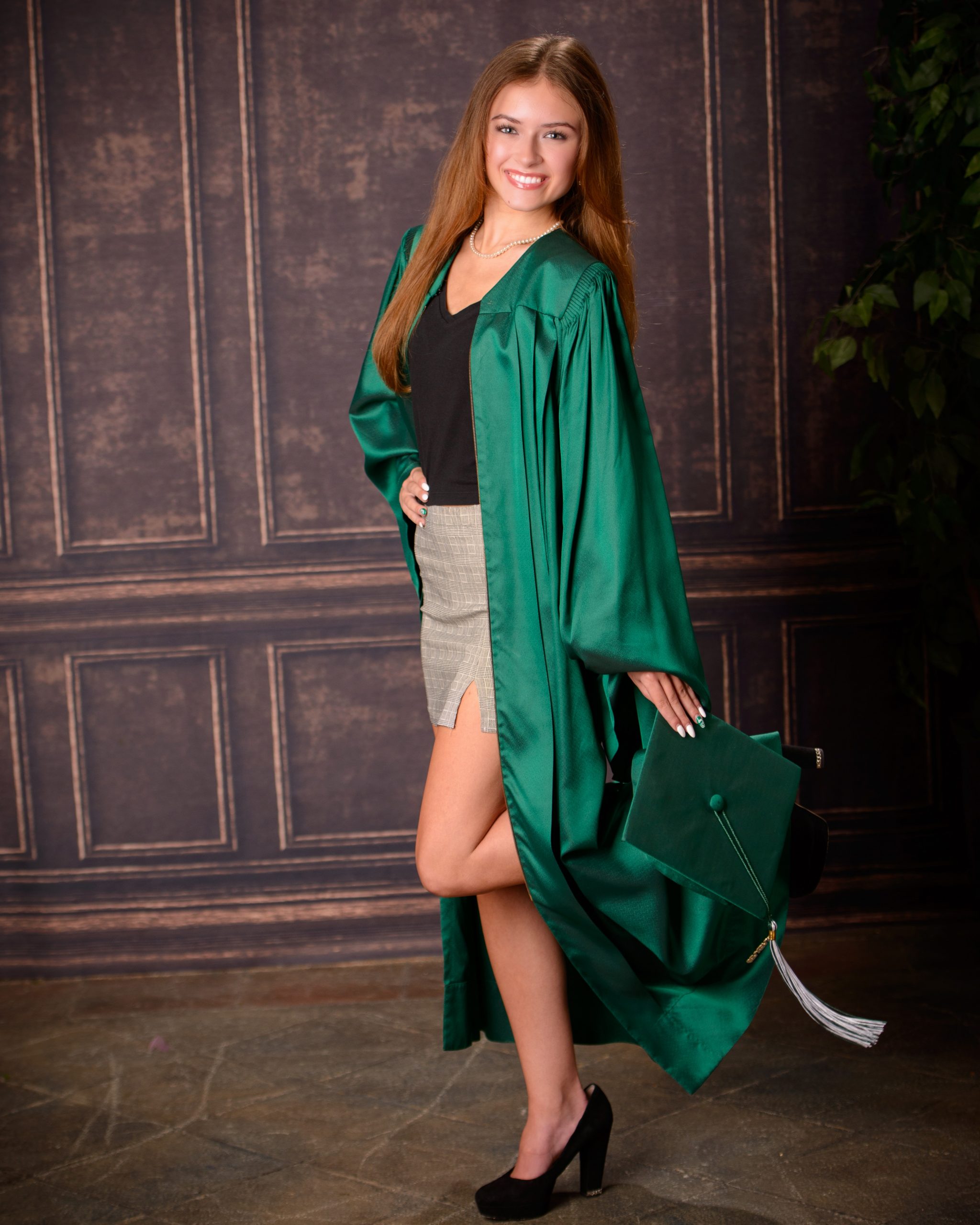 Senior photo session featuring green graduation cap and gown, holding cap in mansion studio setting