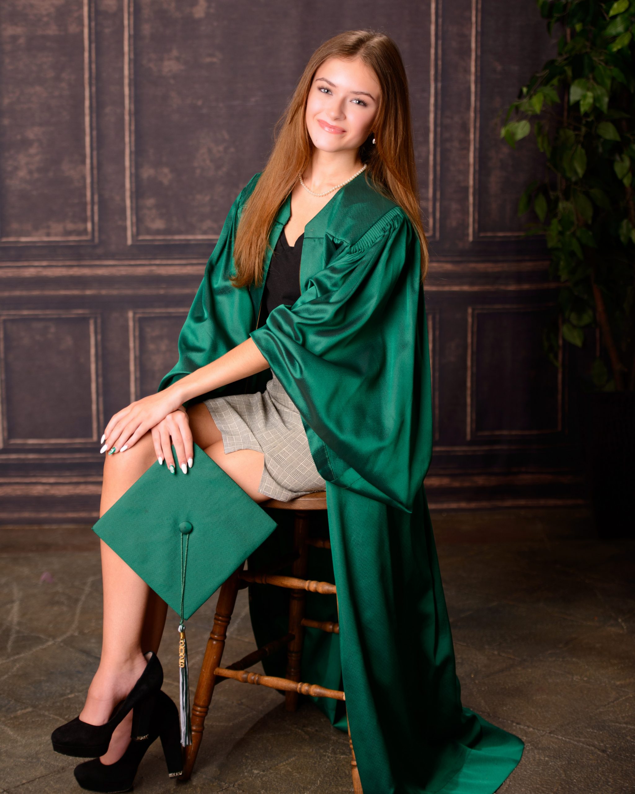 Senior photo session featuring green graduation cap and gown, holding cap in mansion studio setting