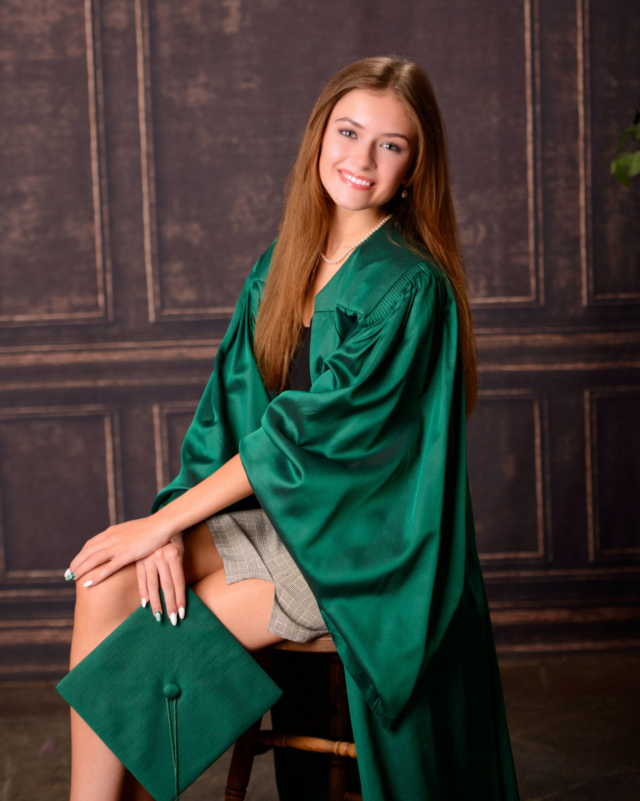 Senior photo session featuring green graduation cap and gown, holding cap in mansion studio setting