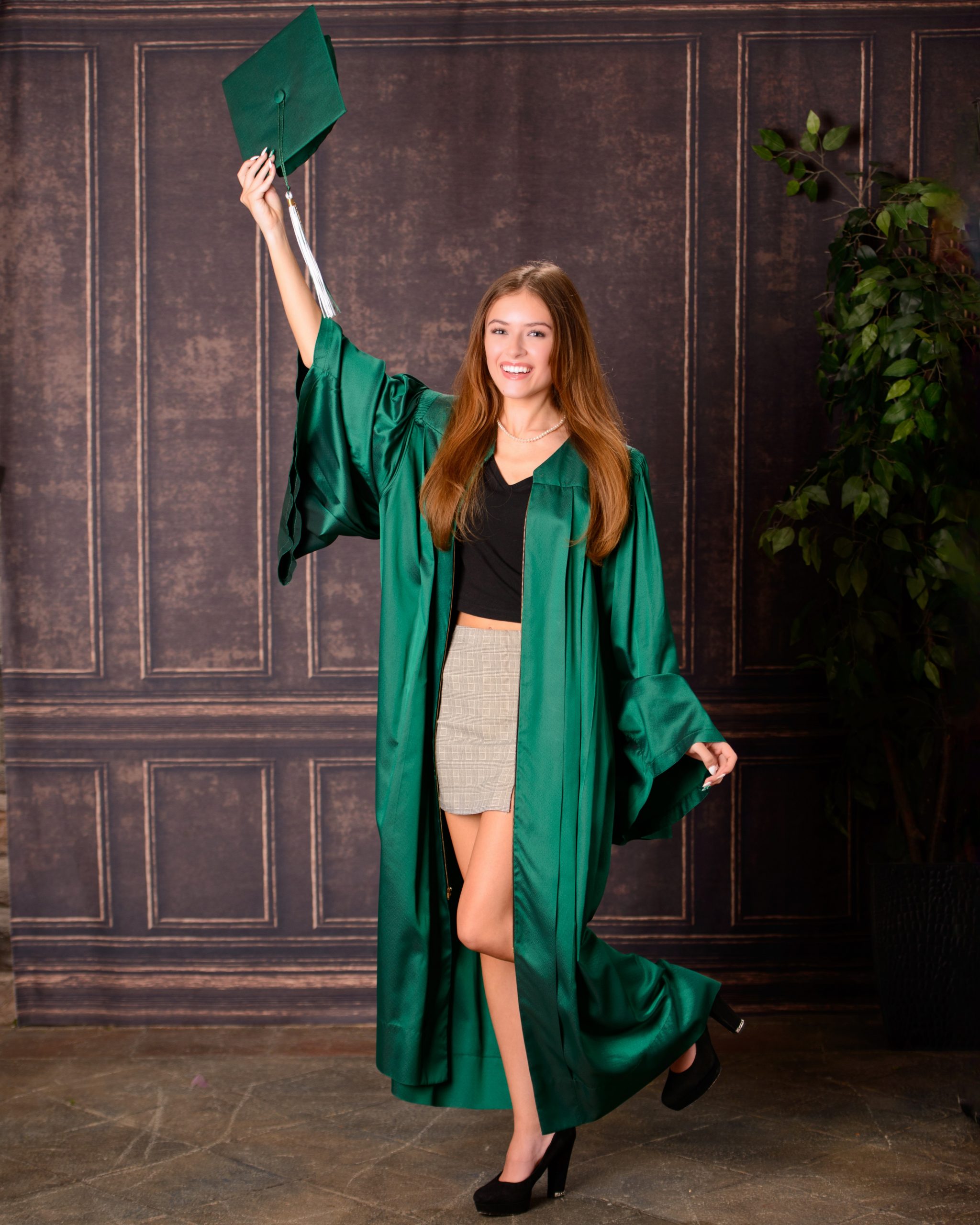 Senior photo session featuring green graduation cap and gown, holding cap in mansion studio setting