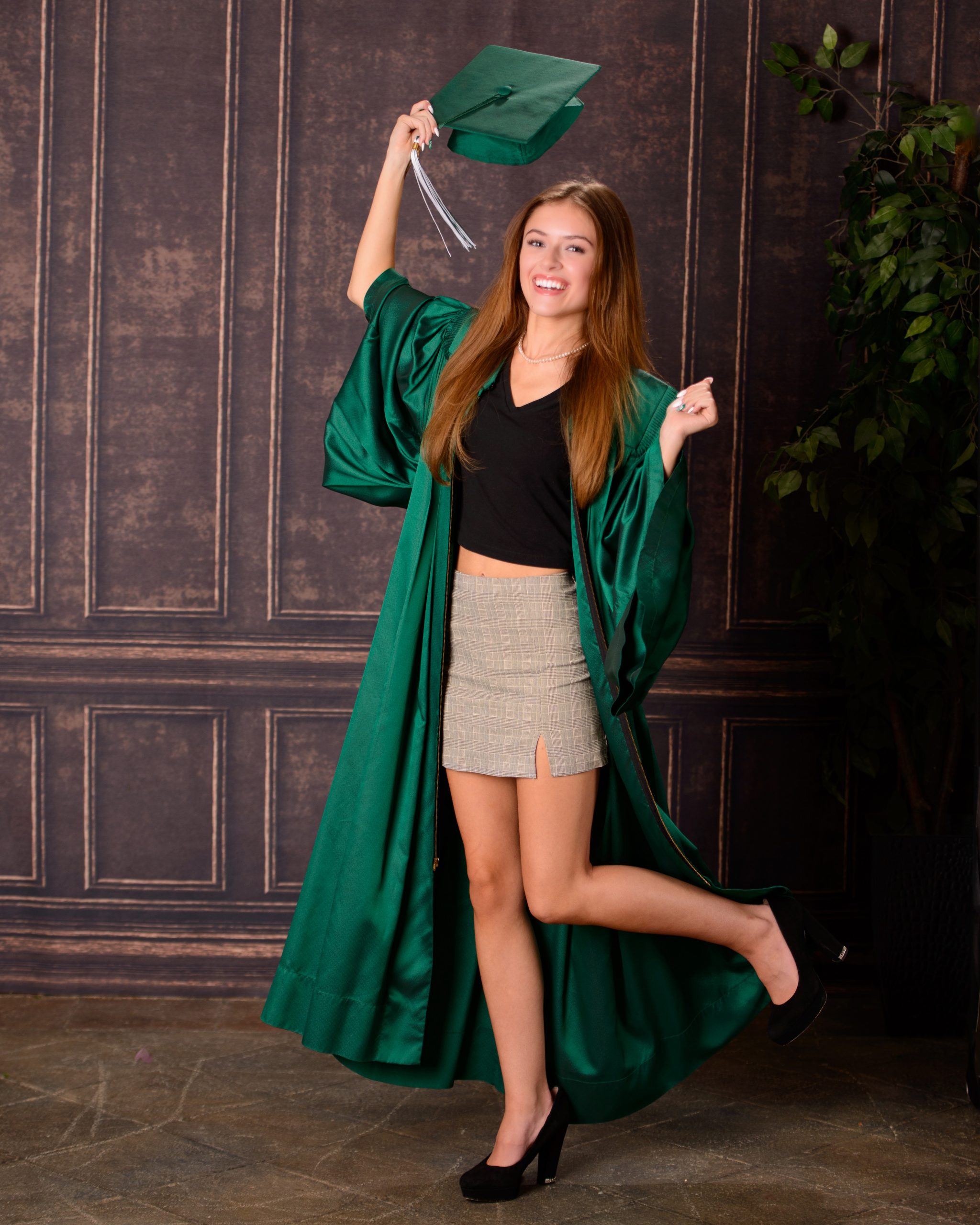 Senior photo session featuring green graduation cap and gown, holding cap in mansion studio setting