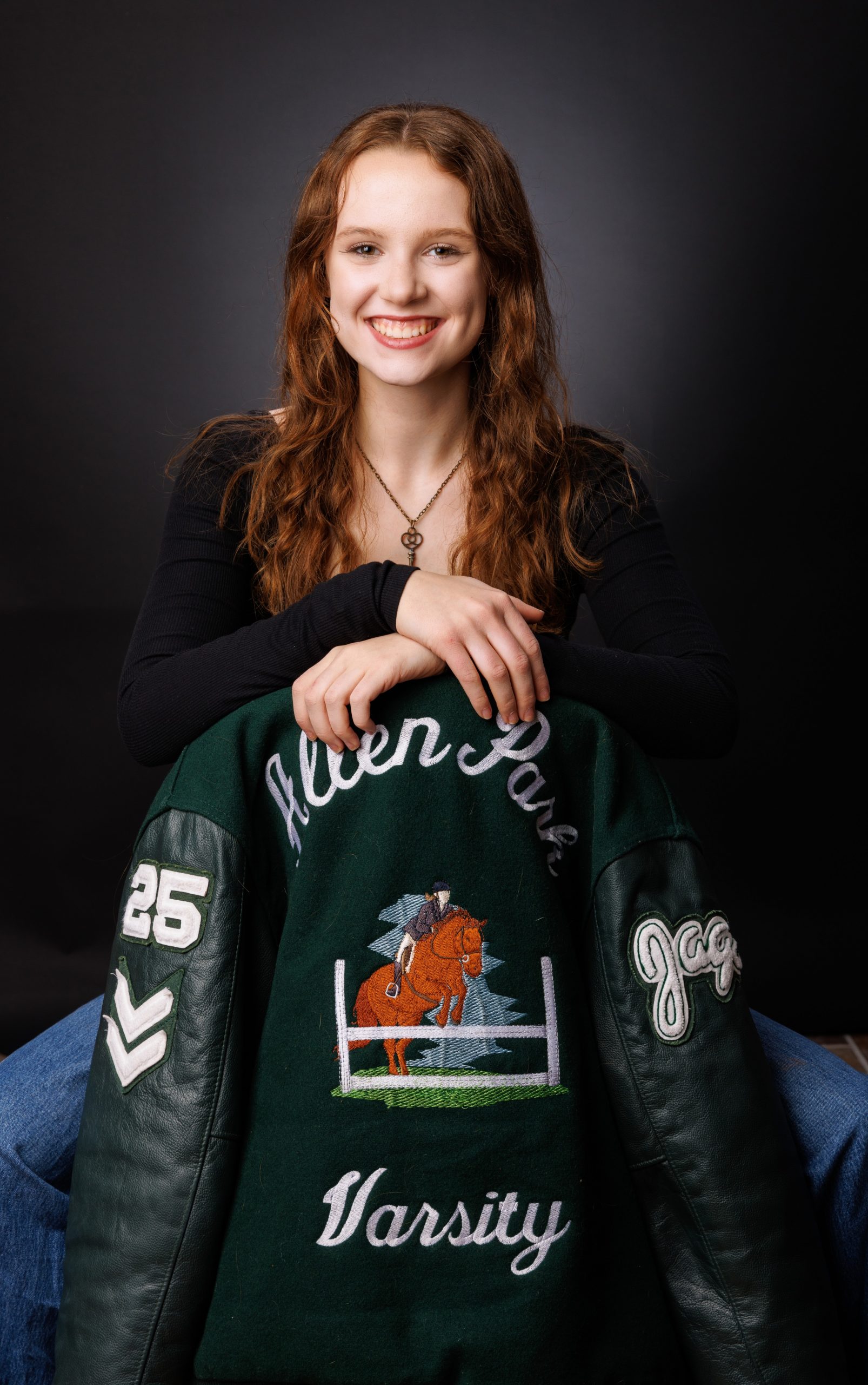 Female student holding Allen Park Varsity jacket with equestrian design in studio session