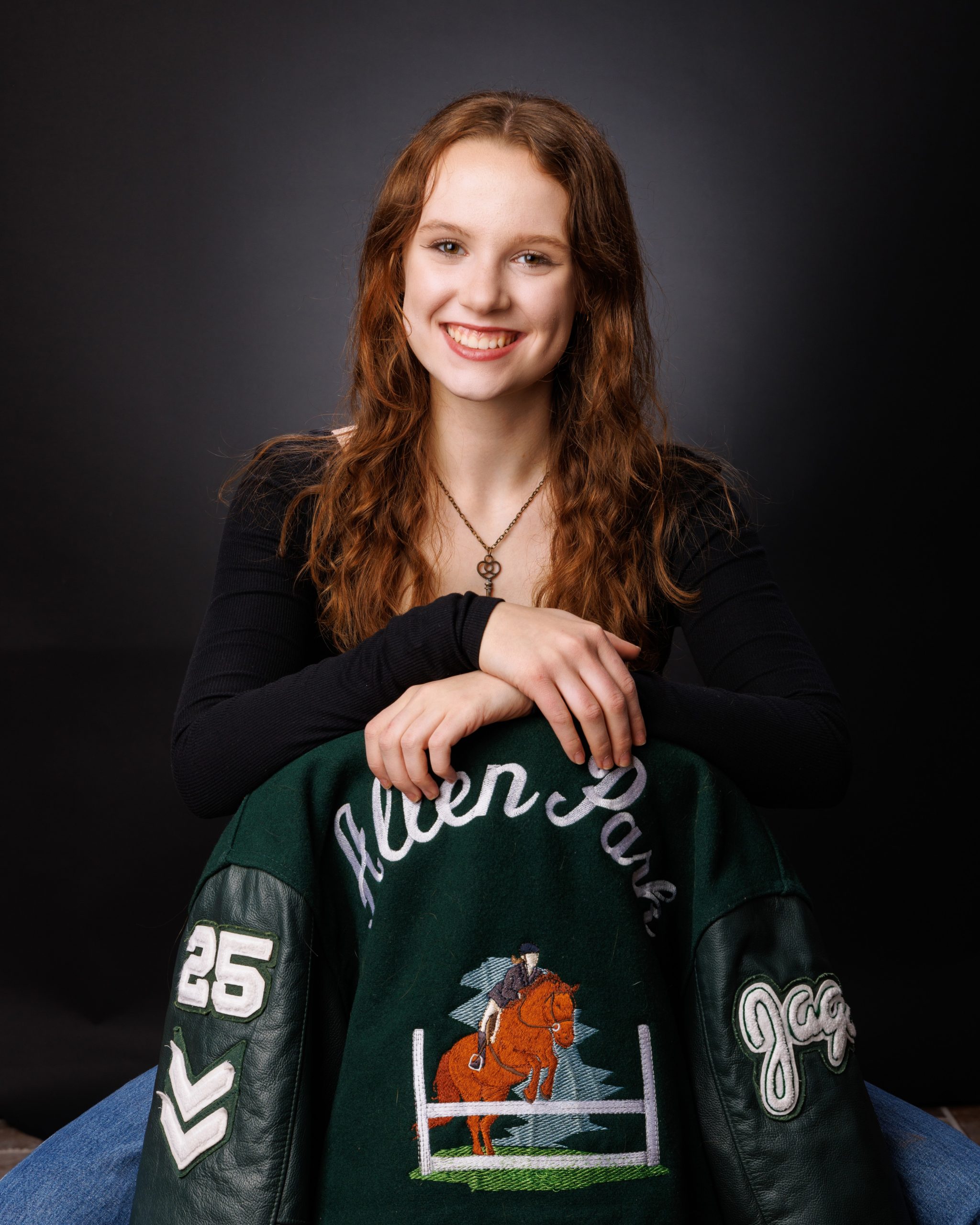 Female student holding Allen Park Varsity jacket with equestrian design in studio session