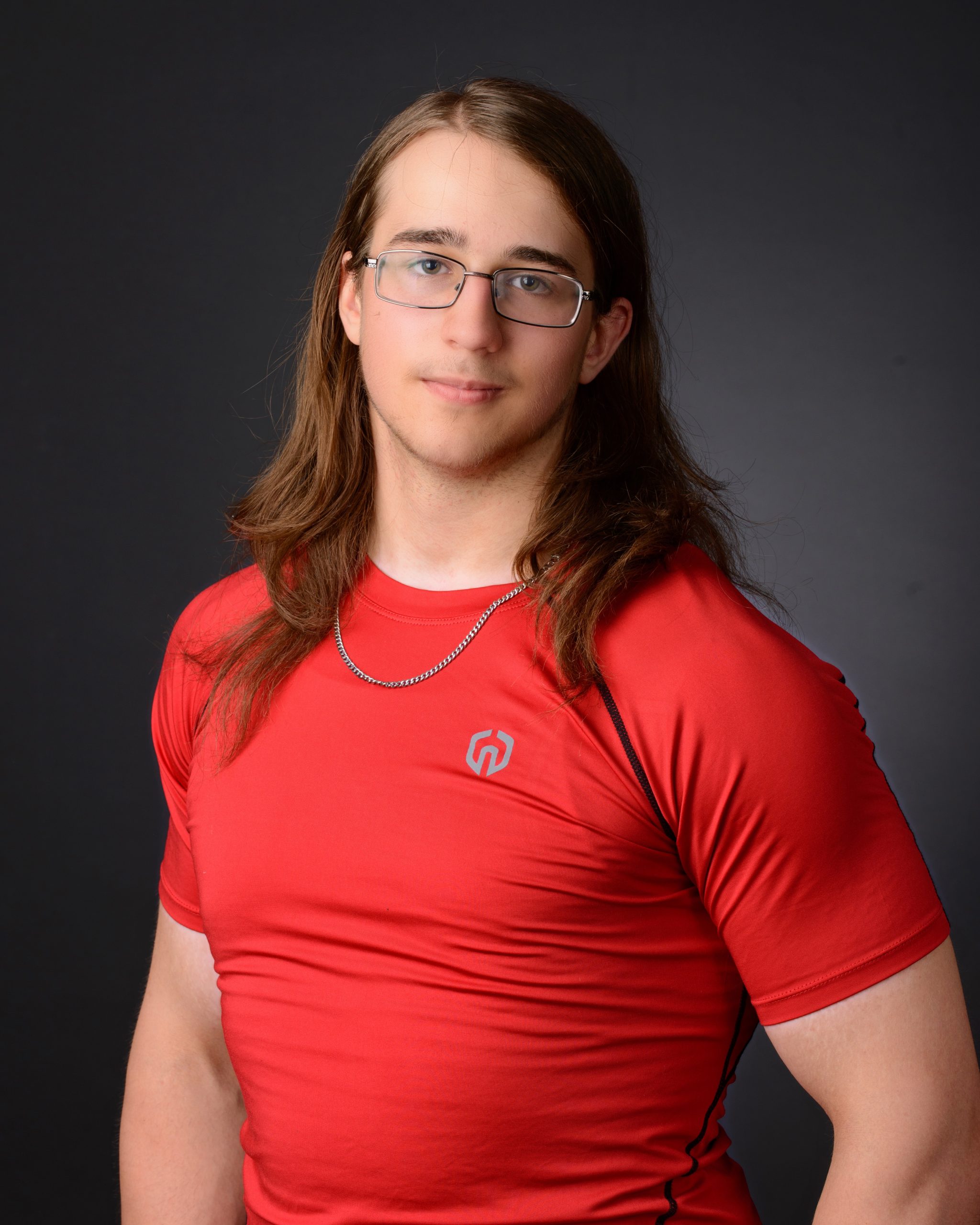 high school senior athlete in red compression shirt, long hair, glasses, posing with one hand raised