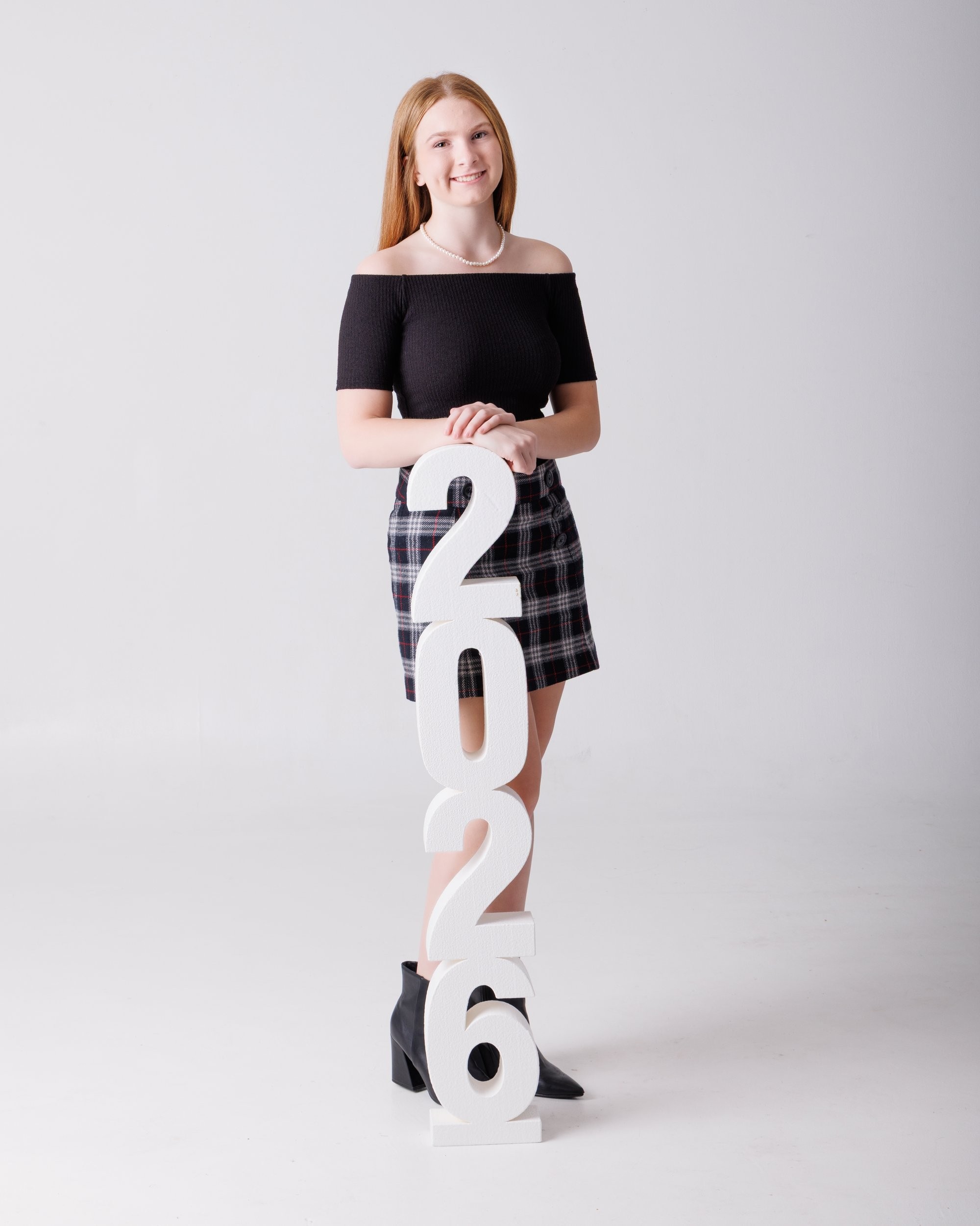 Bailey holds large '2026' numbers while standing in a white studio setting for her senior photography shoot