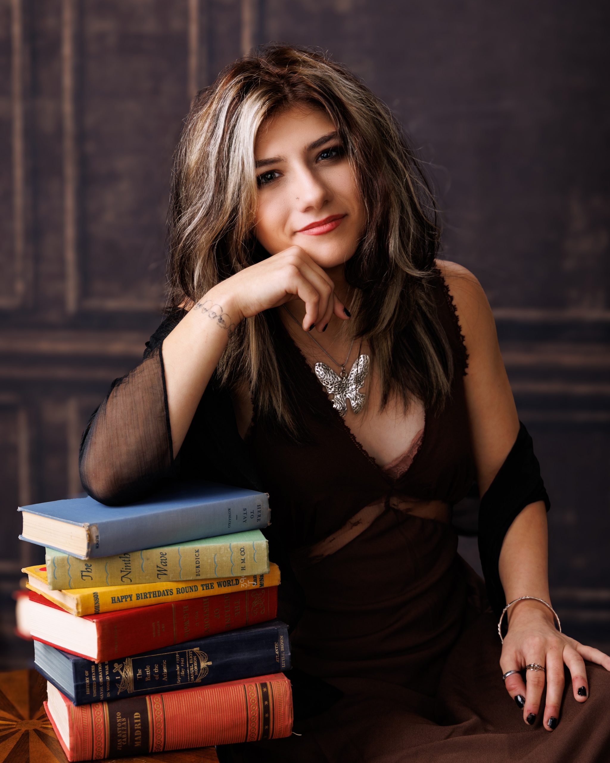 Brooke seated with stacked books in green chair for a Downriver senior photography shoot at Studio ONE