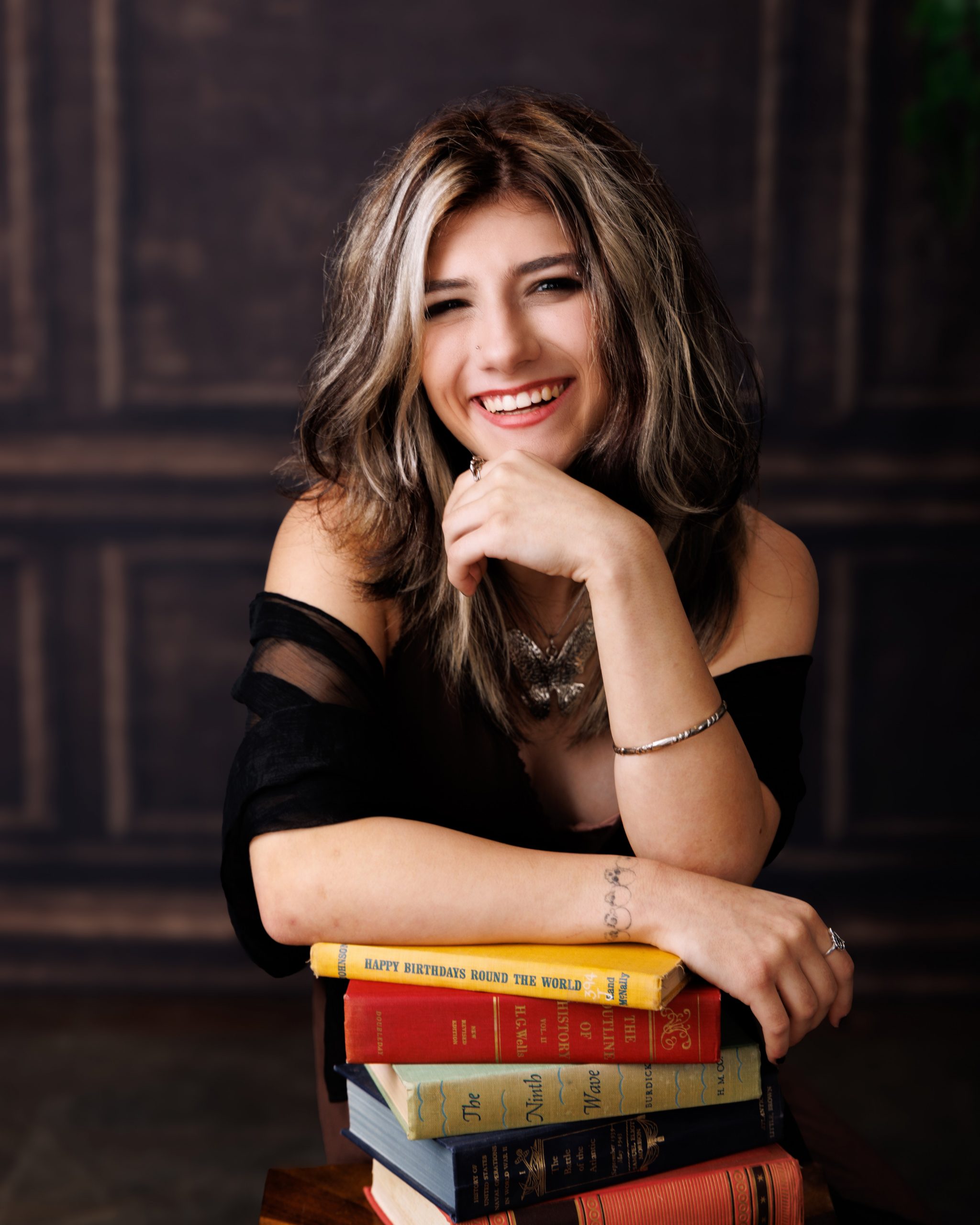 Brooke seated with stacked books in green chair for a Downriver senior photography shoot at Studio ONE