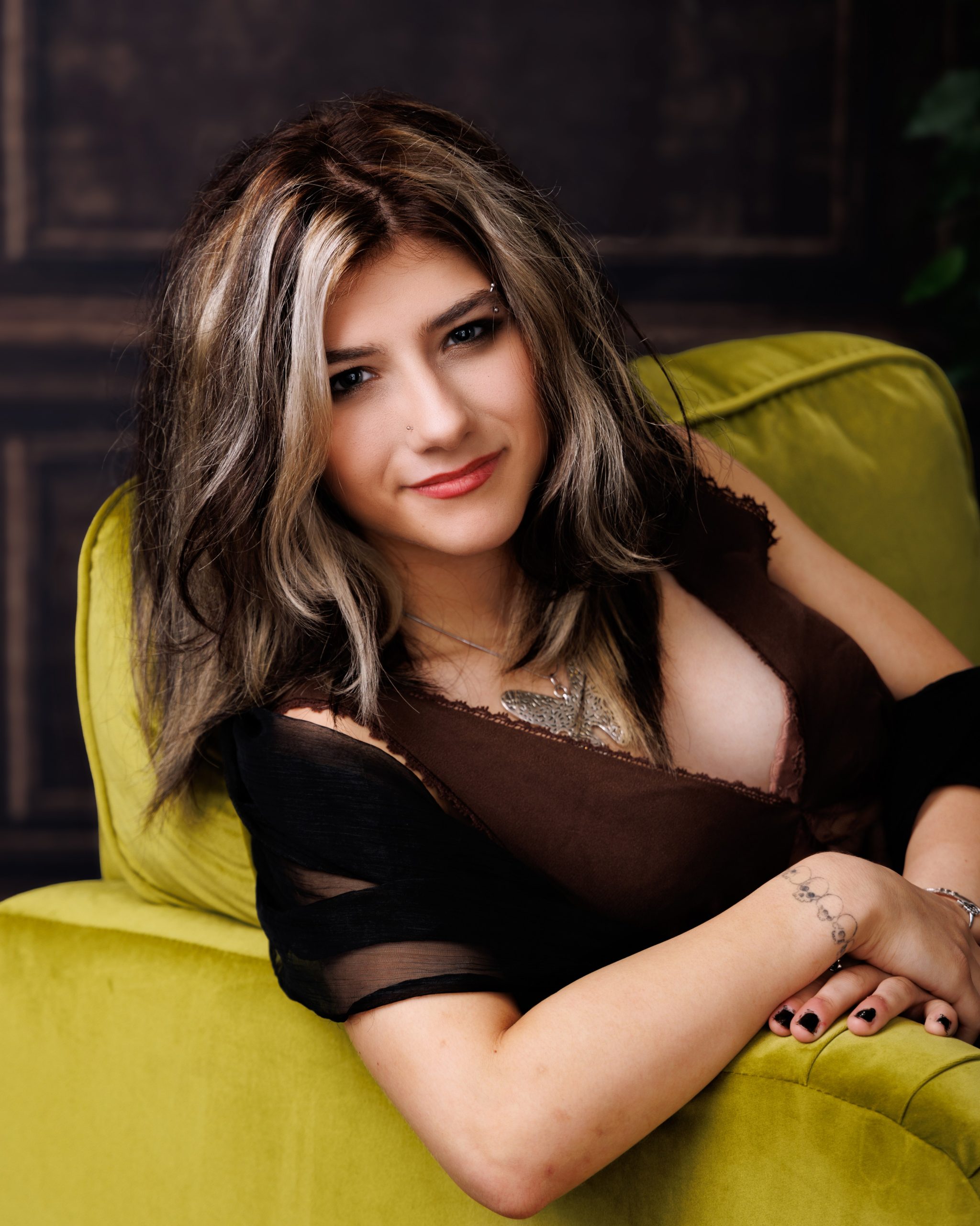 Brooke seated with stacked books in green chair for a Downriver senior photography shoot at Studio ONE