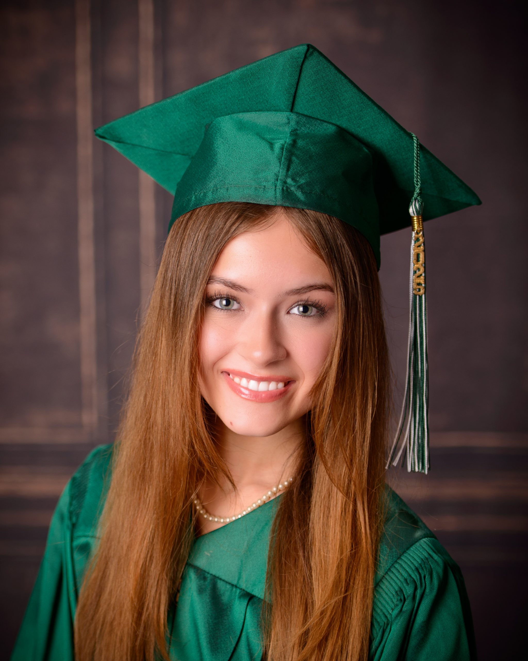 Senior graduate posing with cap held up, wearing green gown and black heels