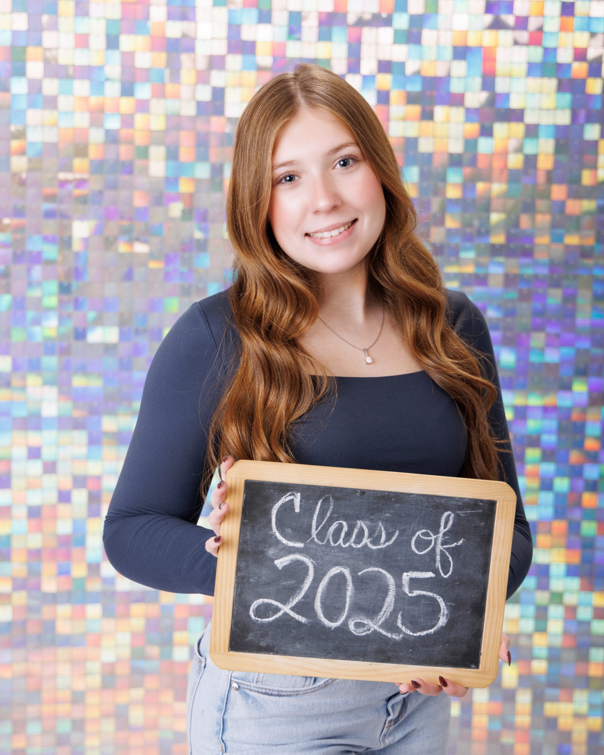 Senior portrait of student holding 'Class of 2025' sign against glitter wall backdrop