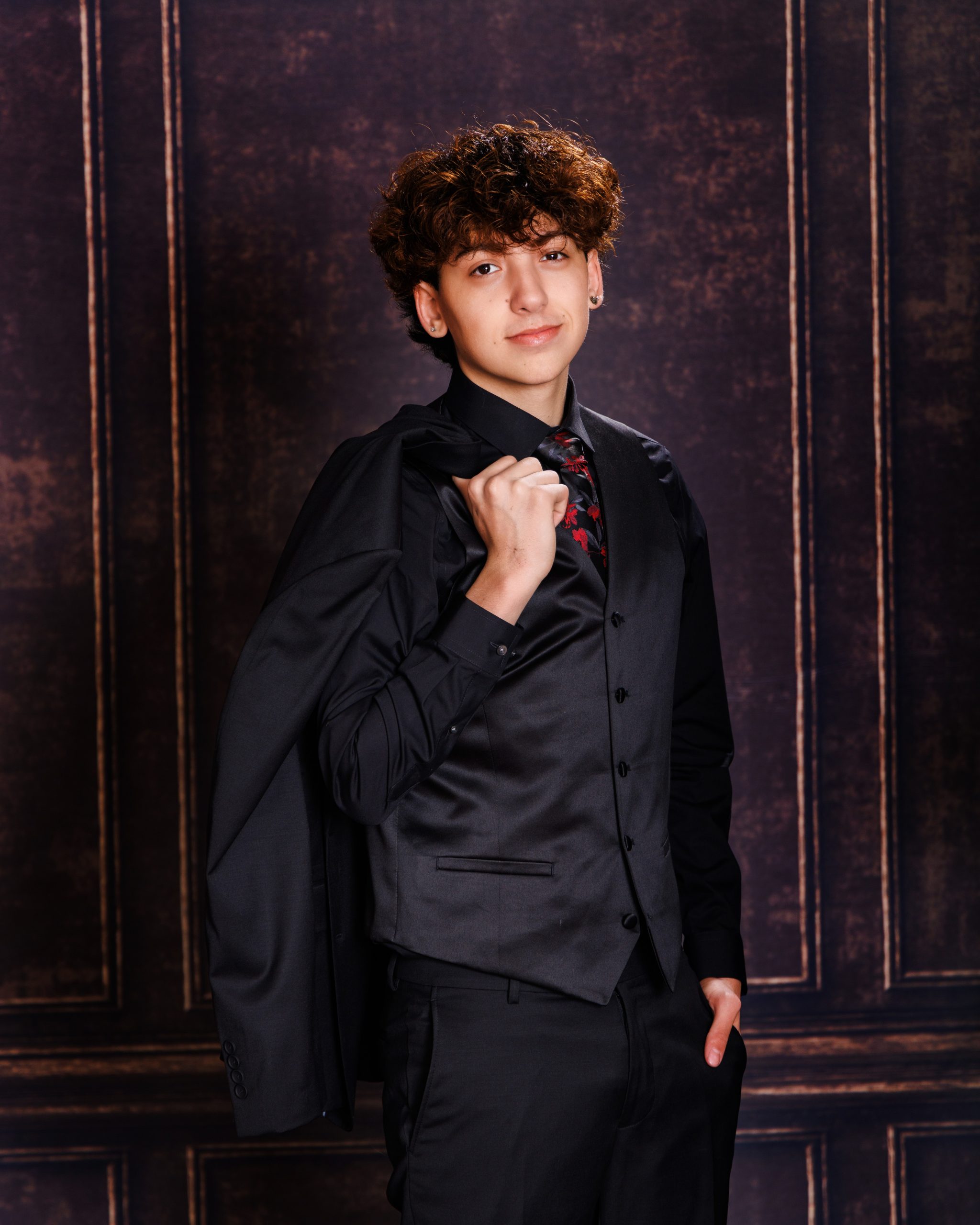 Diego wearing green varsity jacket with 'Diego' embroidery, black shirt and tie, studio portrait