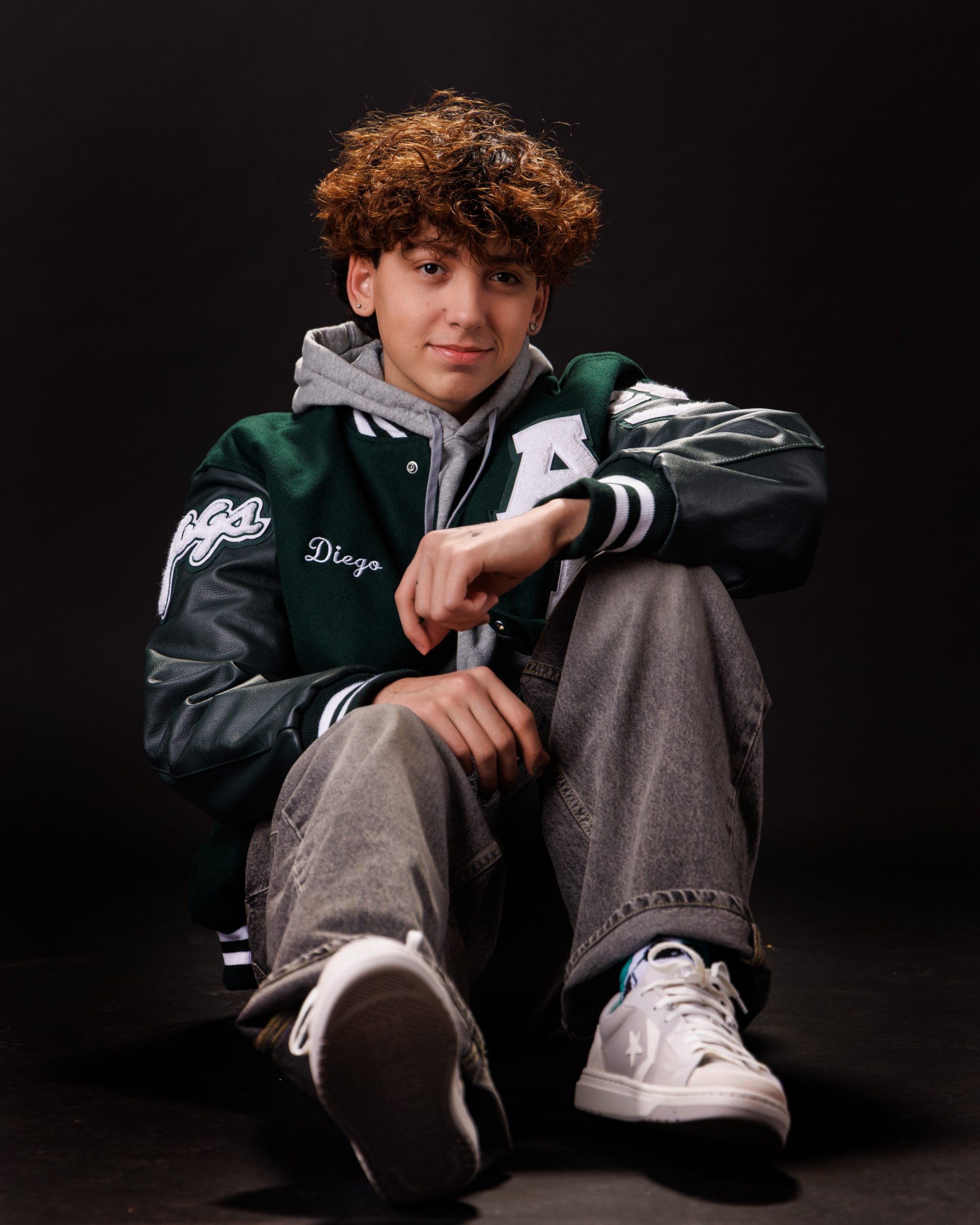 Diego seated on wooden bench in red hoodie, white tee, weathered door background