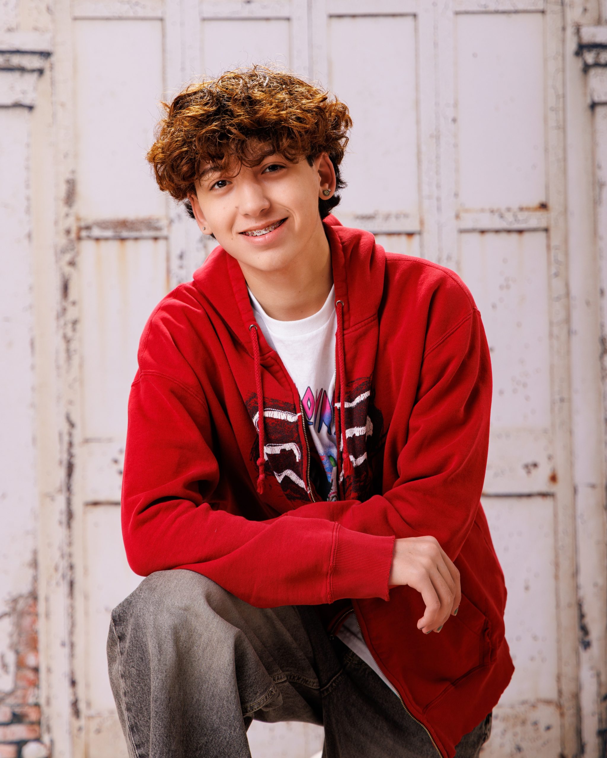 Diego seated on wooden bench in red hoodie, white tee, weathered door background