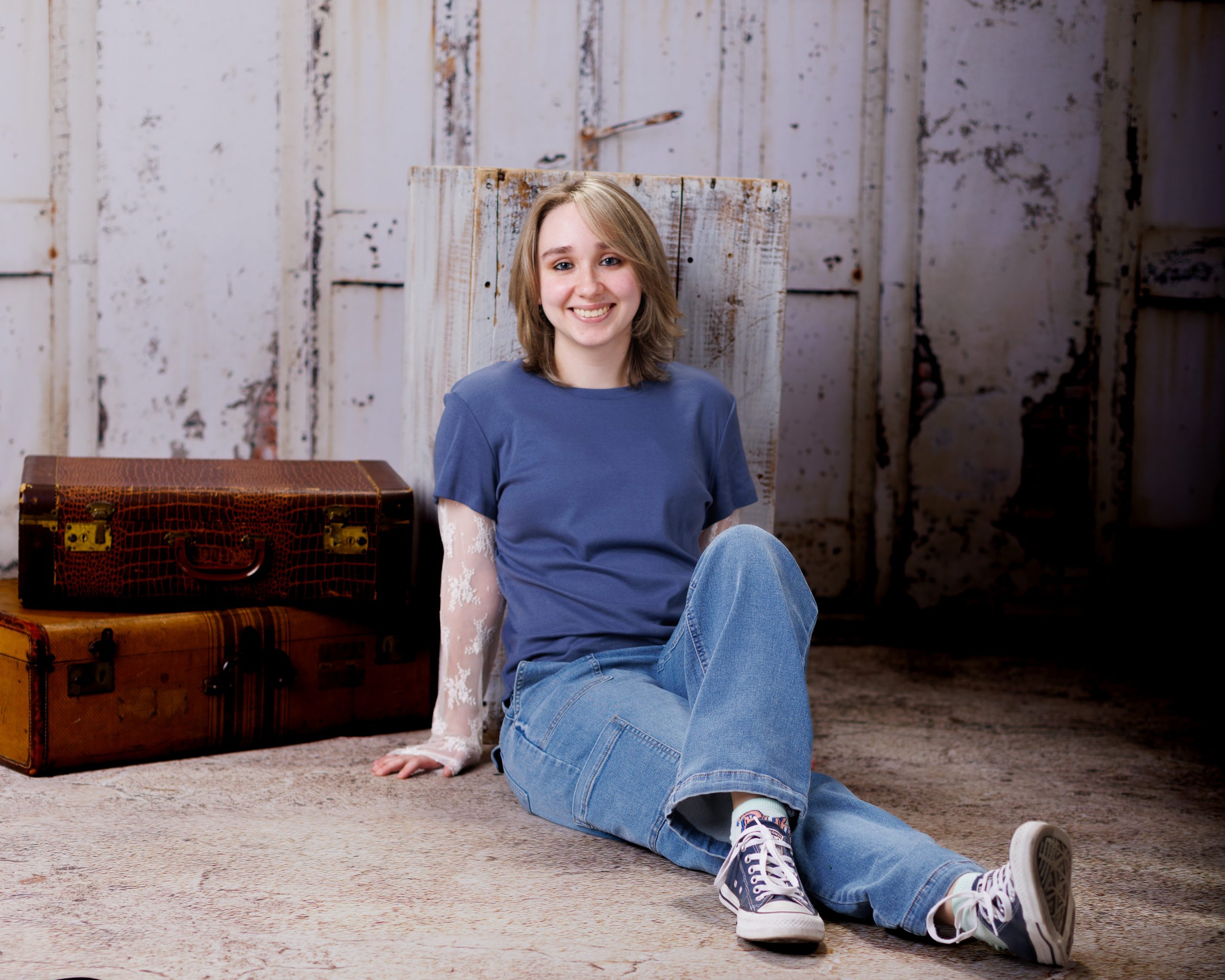 Emma seated with vintage luggage and rustic background for Downriver photography