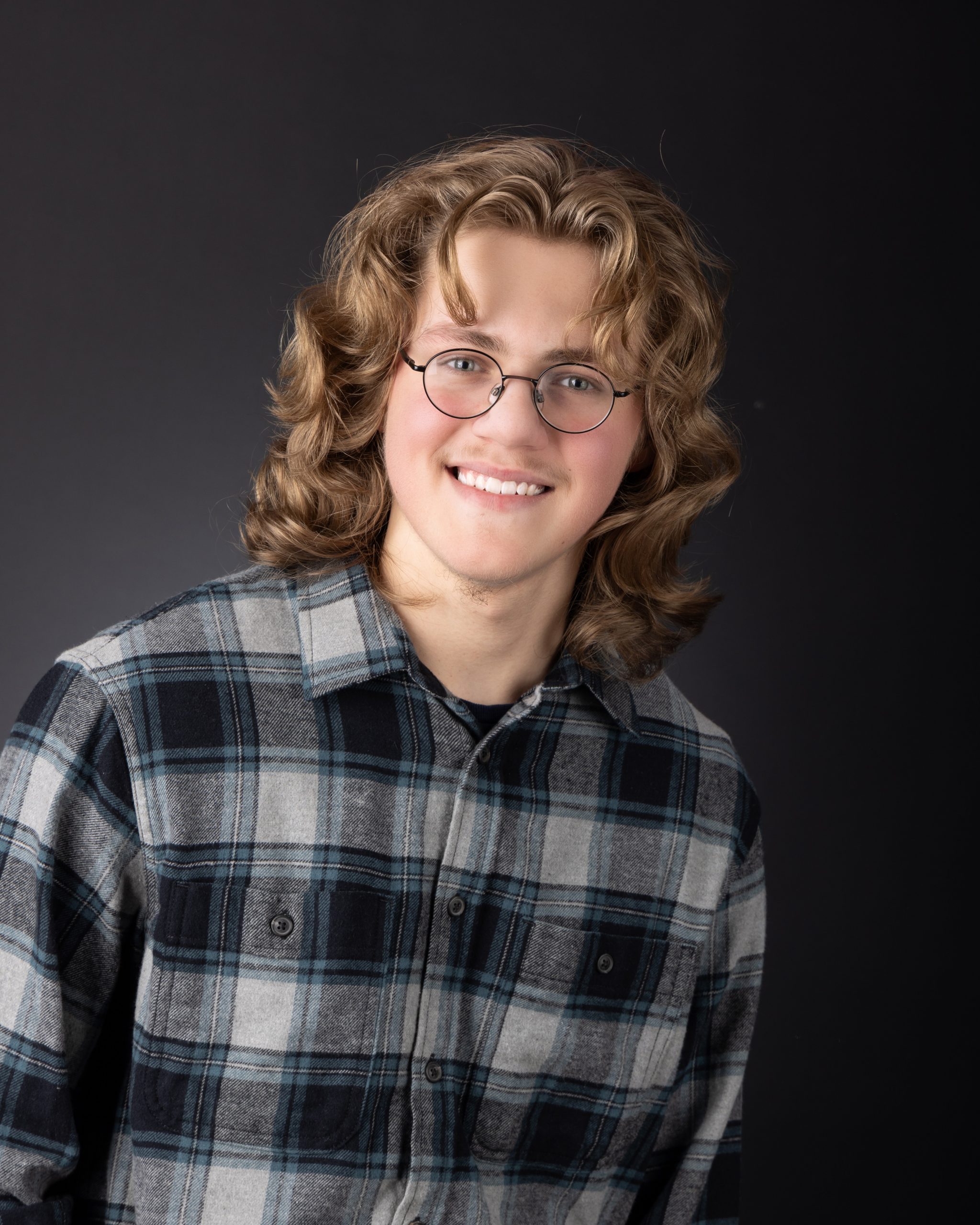 Allen Park senior portrait of Gavin in plaid shirt and glasses against dark background