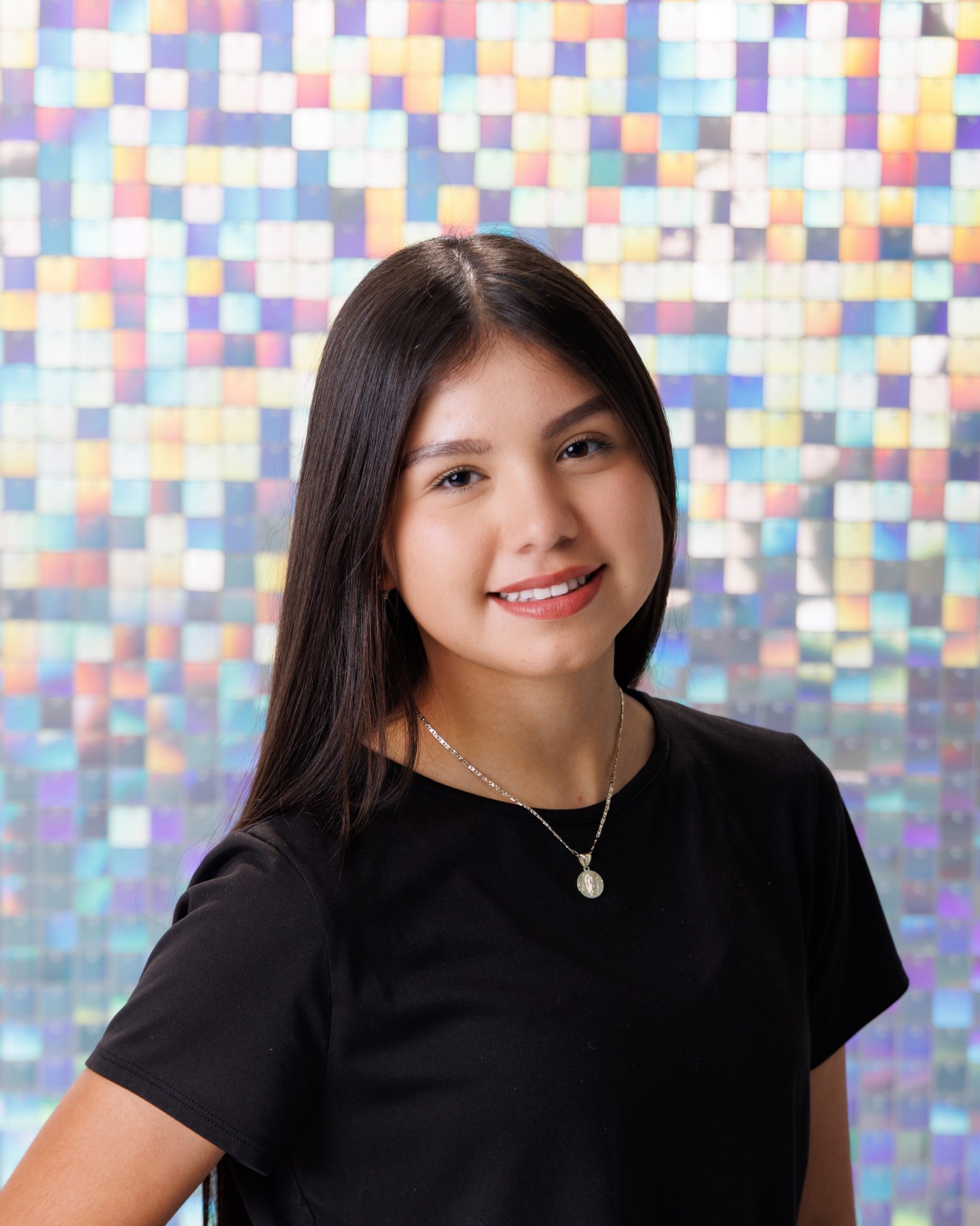 Senior girl Anahi posing on pink chair with white fluffy pillow against glitter pixel wall background