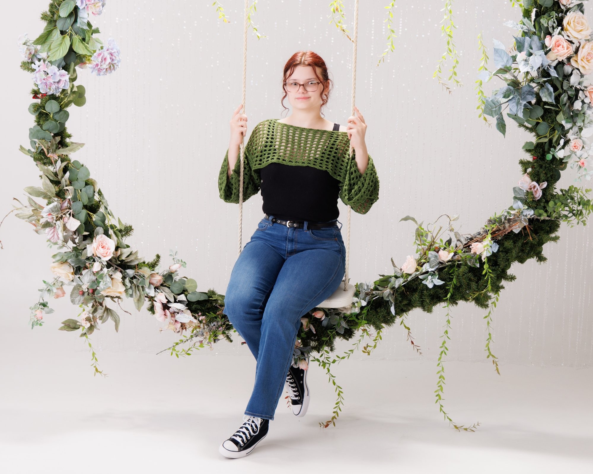 Grace standing confidently in front of a large floral wreath arch for senior photography session