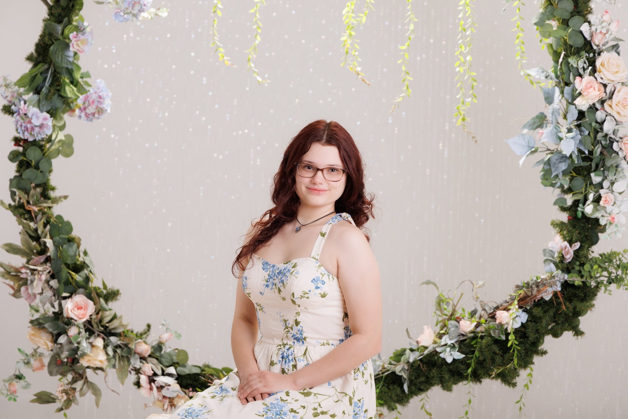 Senior portrait of Grace wearing a blue and green floral dress against a stone wall backdrop
