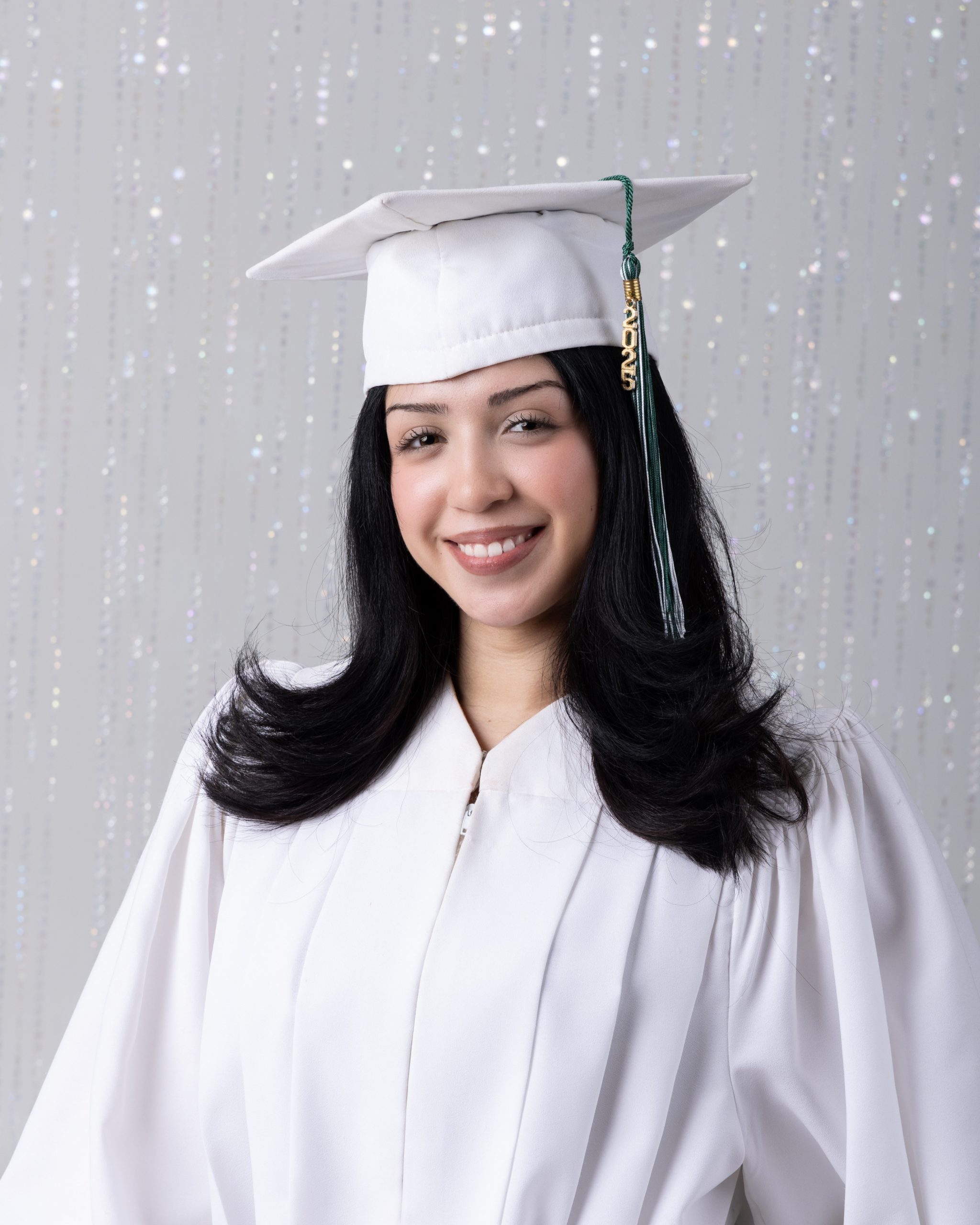 Graduation-ready senior photo featuring a student in white cap, lace cardigan, and black dress against light pink backdrop