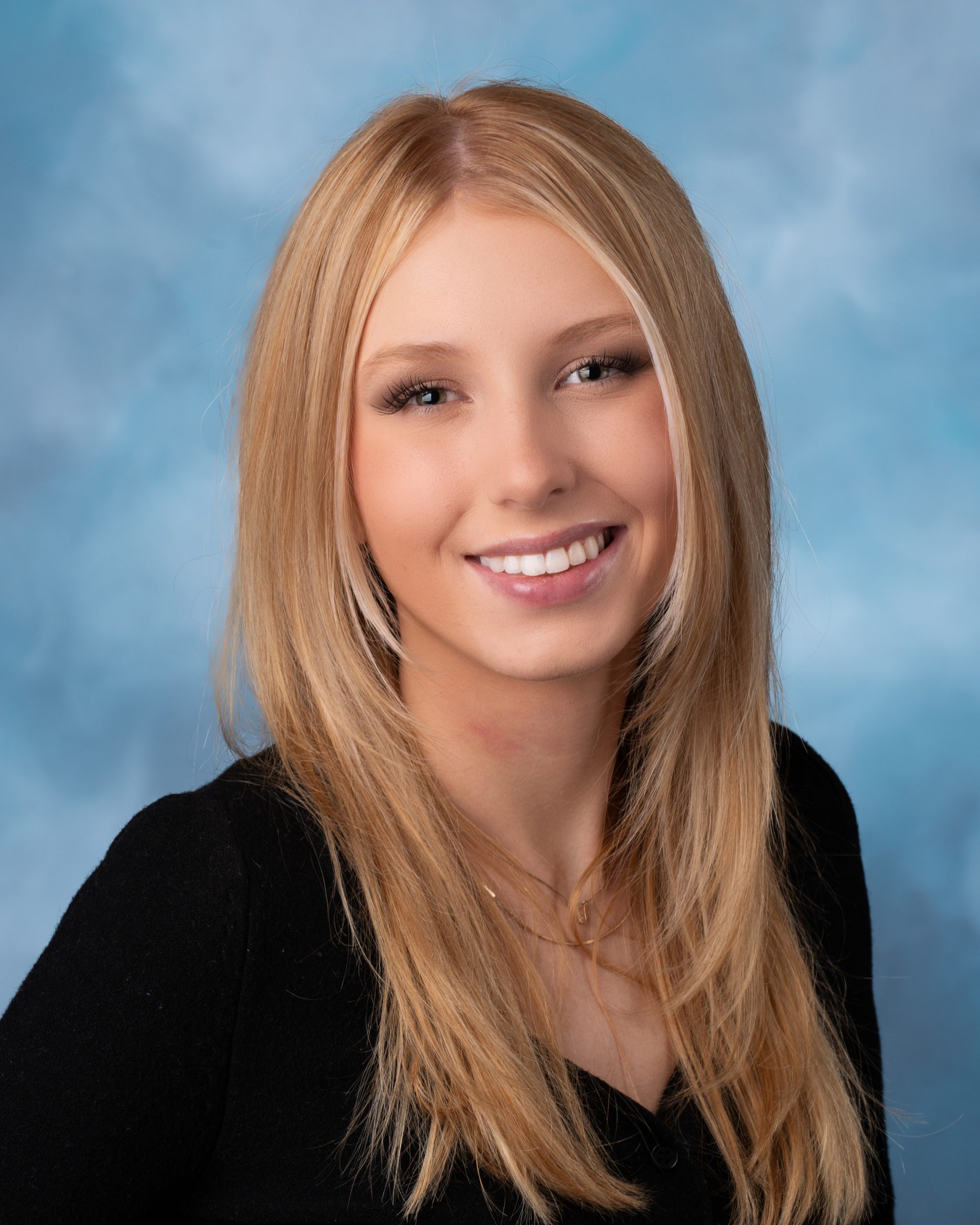 Senior portrait photography session featuring a smiling blonde woman with long hair against a blue backdrop