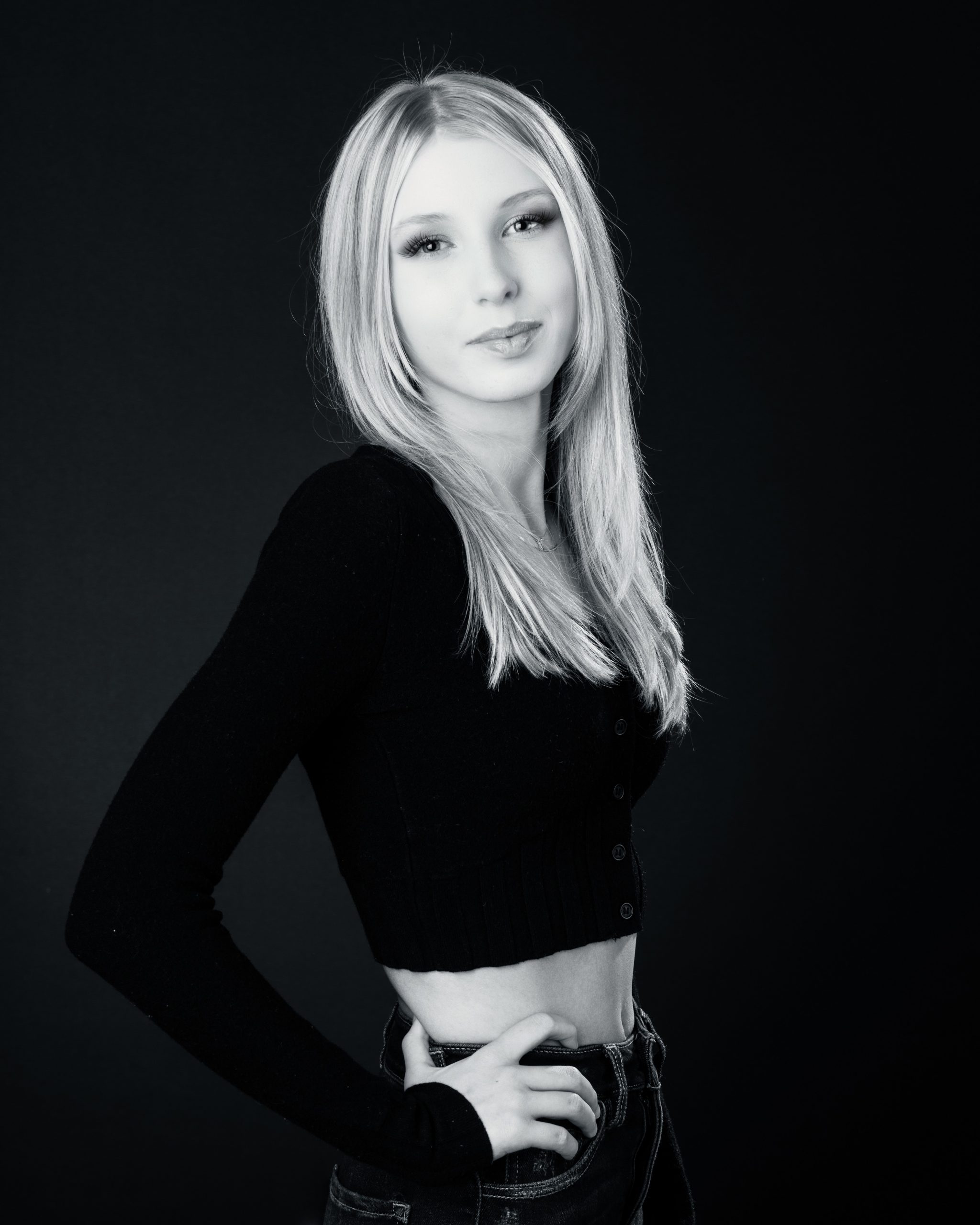 Professional senior headshot of a young woman in black top against dark background