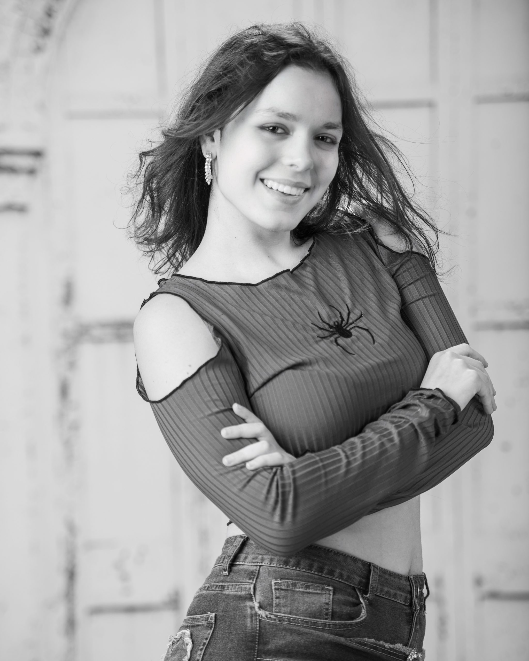 confident senior photo featuring a woman in red off-shoulder top and heart belt detail standing before weathered white doors