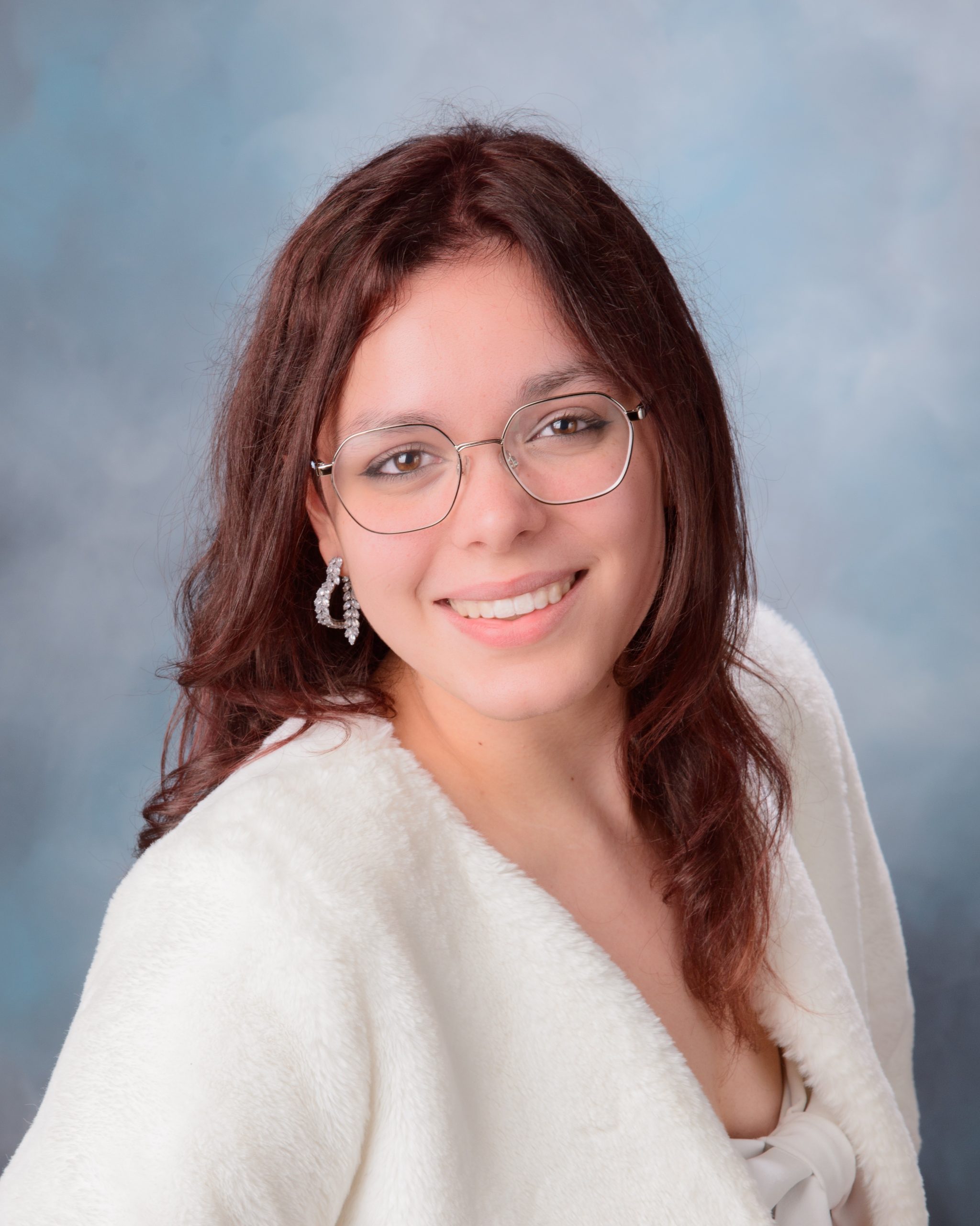 confident senior photo featuring a woman in red off-shoulder top and heart belt detail standing before weathered white doors