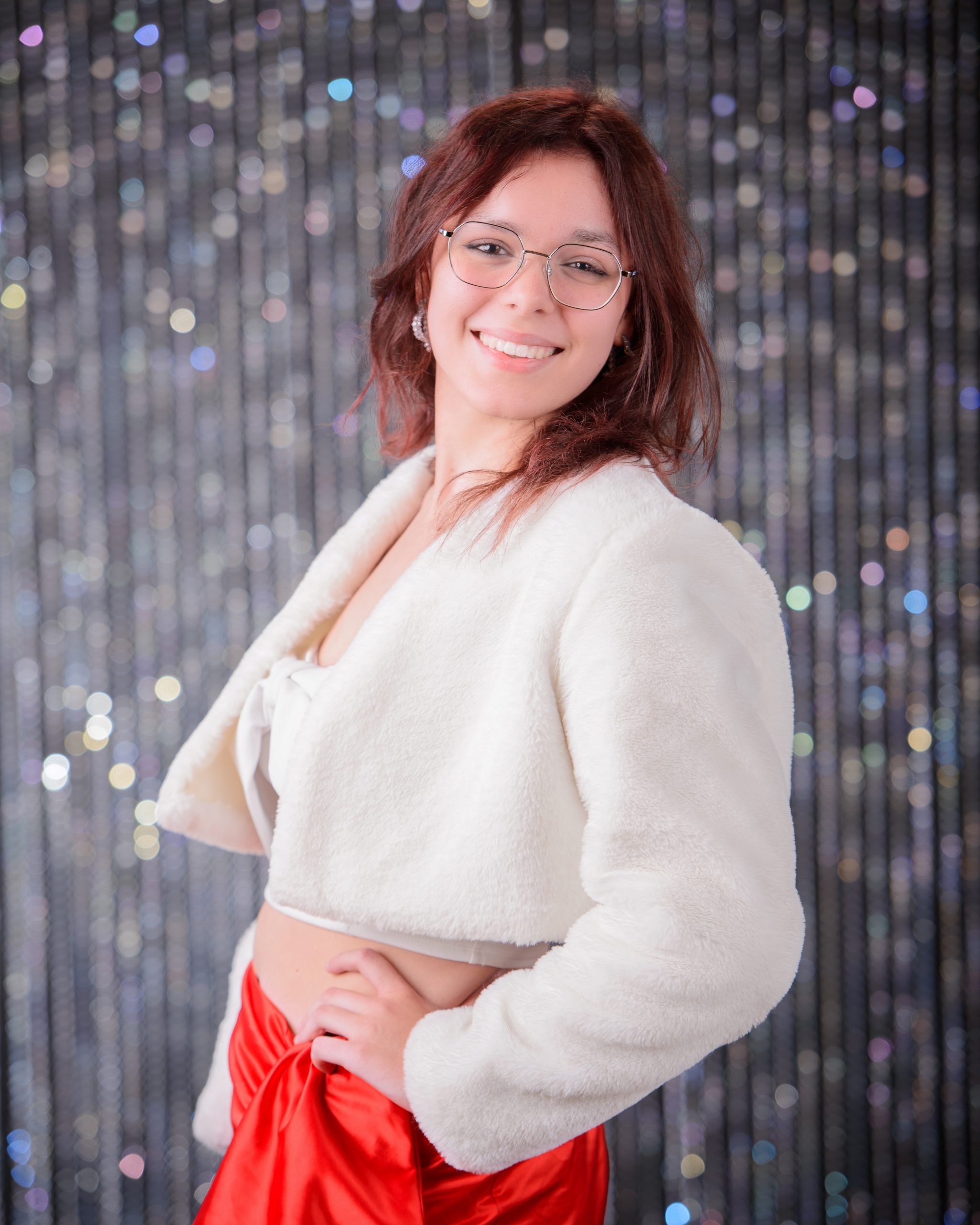 confident senior photo featuring a woman in red off-shoulder top and heart belt detail standing before weathered white doors