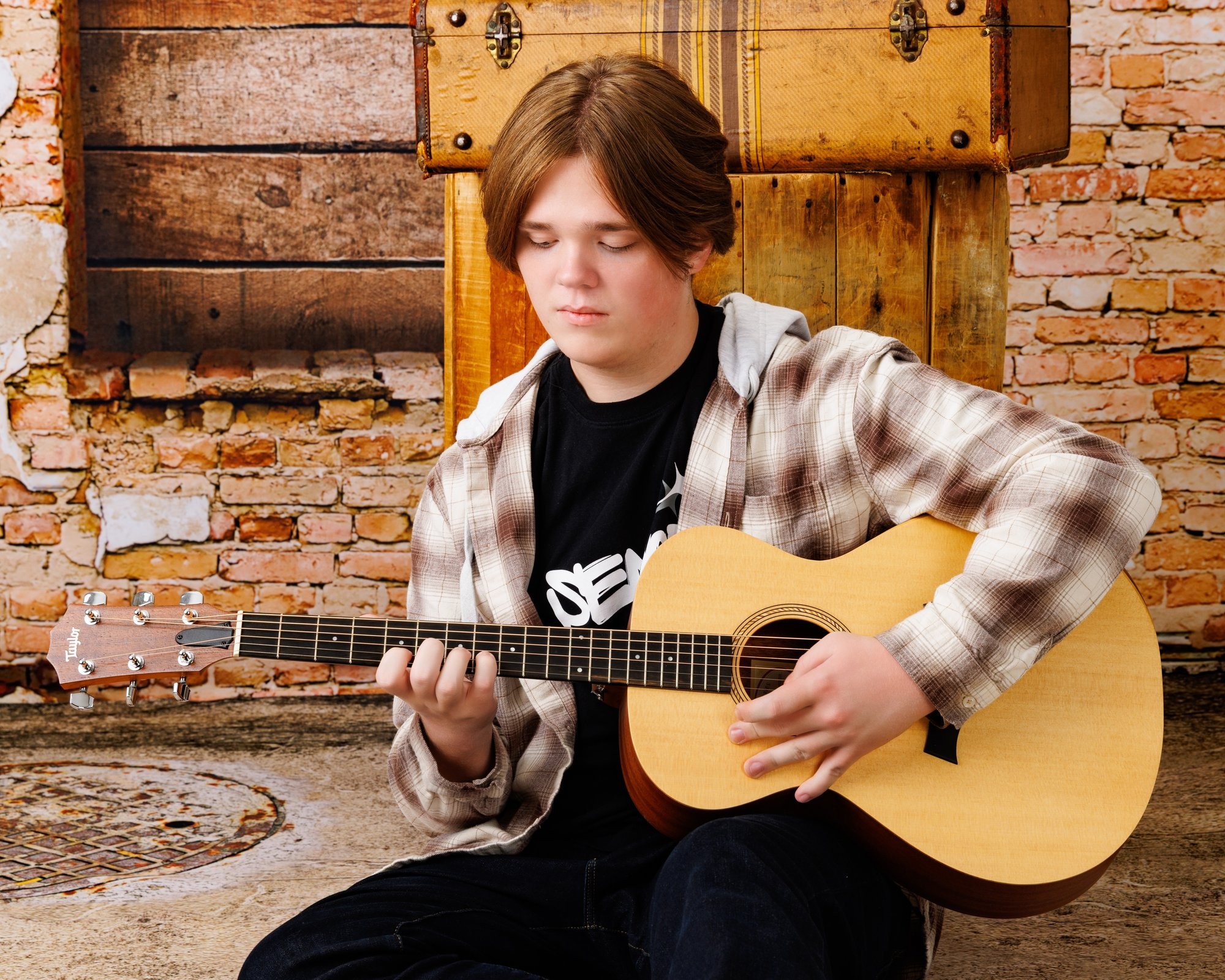 Black-and-white portrait of a guitarist with vintage trunks and brick wall setting for Downriver photography studio