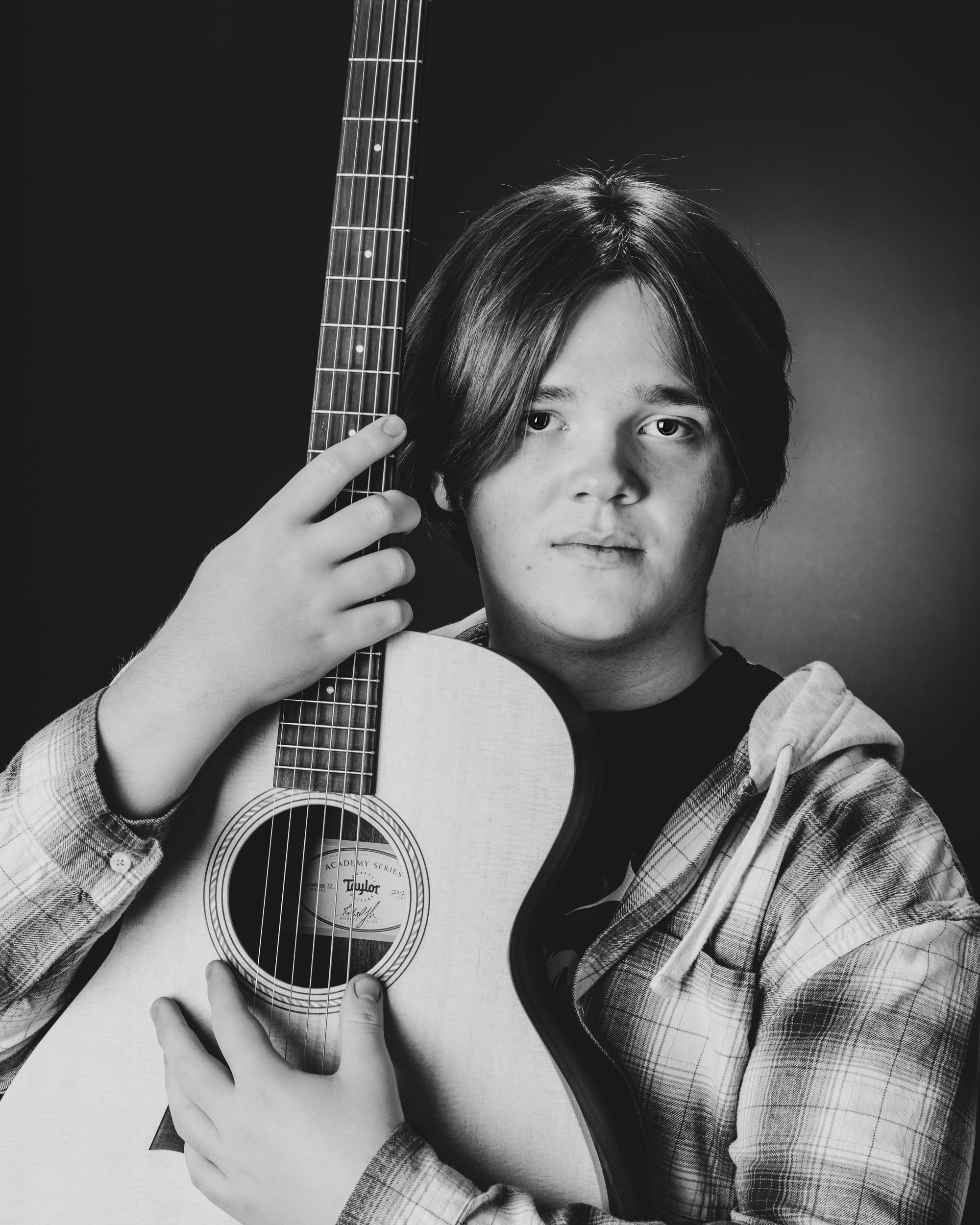 Senior portrait featuring an acoustic guitar against a dark gradient background, showcasing the artist's style in our Taylor photo studio