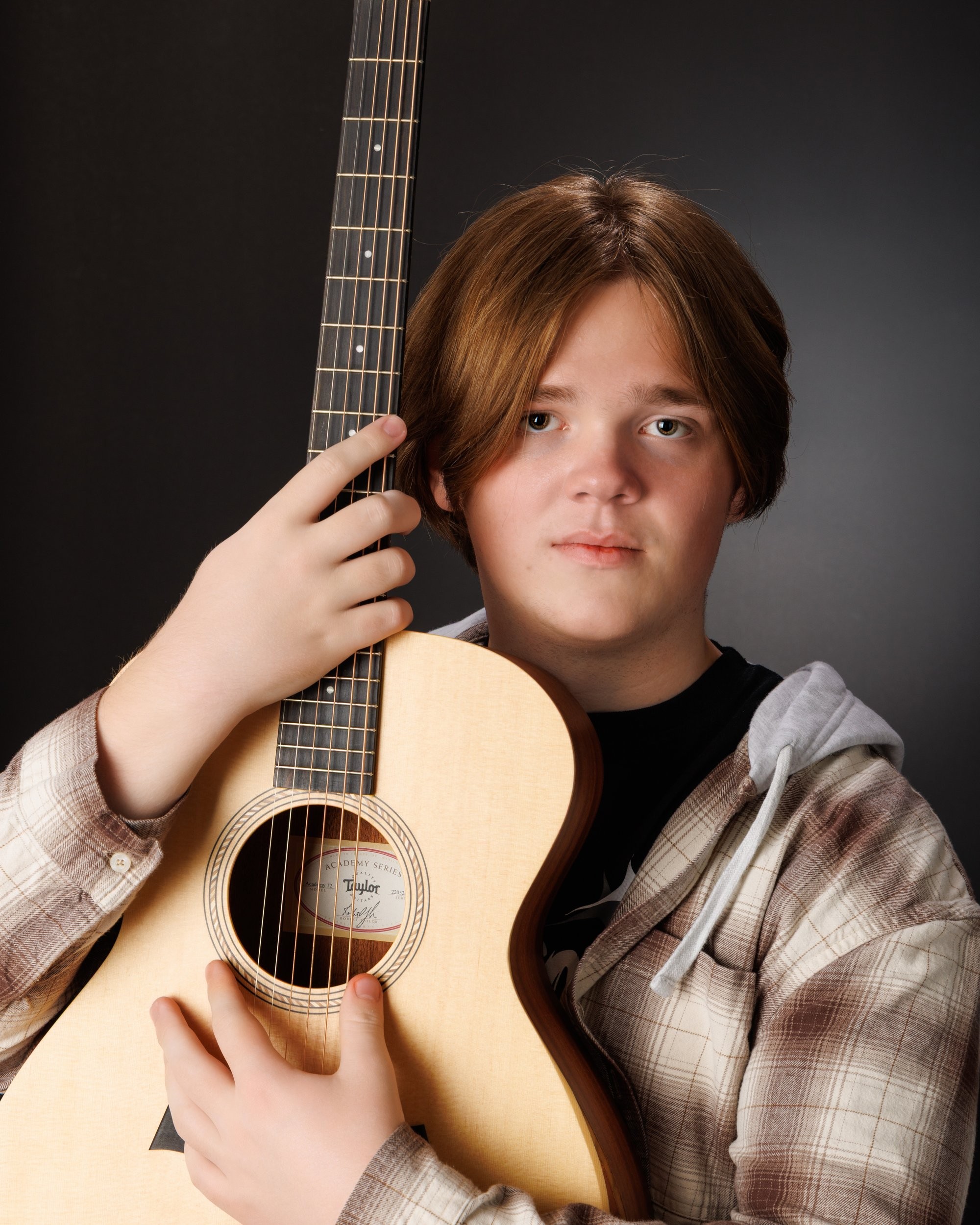Senior portrait featuring an acoustic guitar against a dark gradient background, showcasing the artist's style in our Taylor photo studio