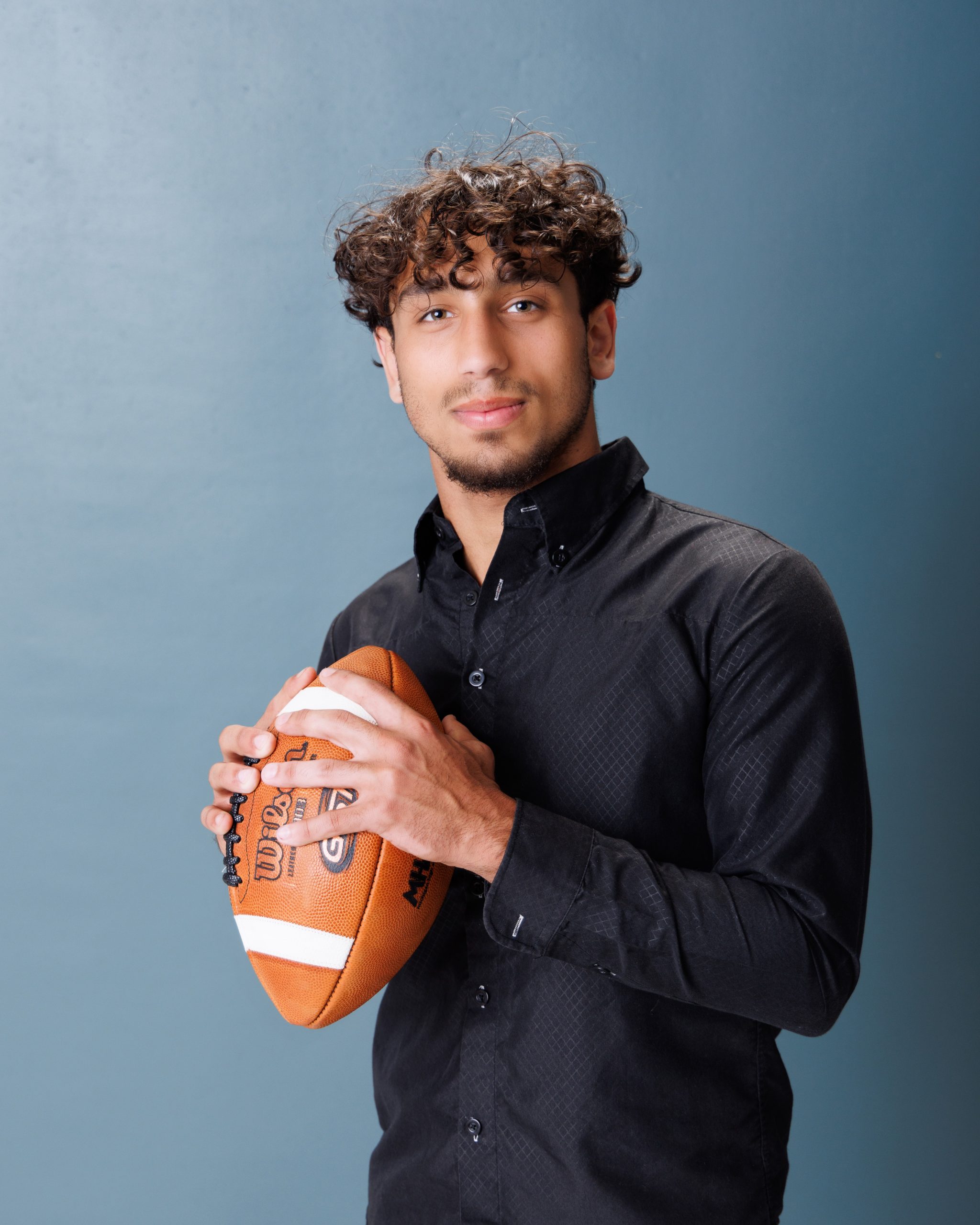 young man posing with football during Allen Park senior photography