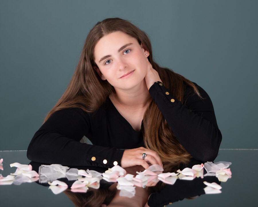 Branna in black top with rose petals on reflective table during Downriver senior photography session