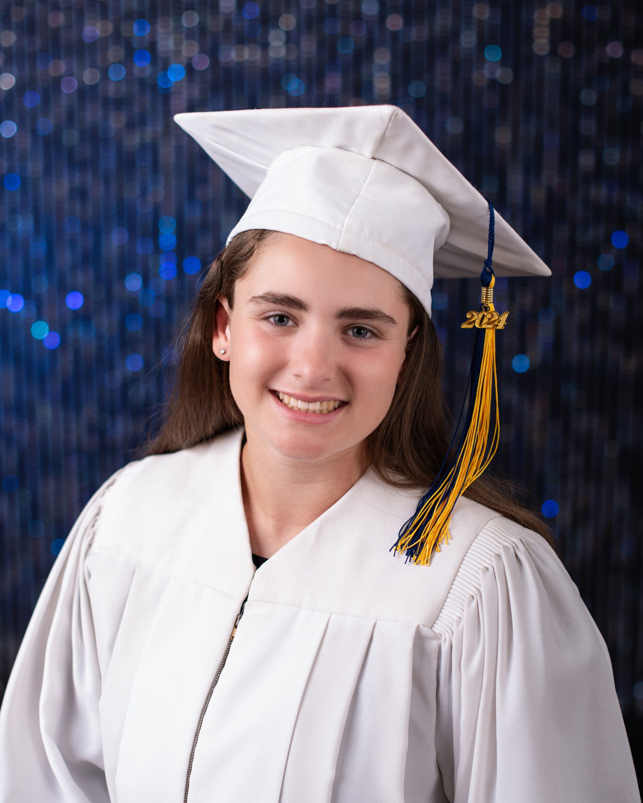Branna wearing graduation cap and gown holding softball bat and ball, sports jerseys in background for senior sports photography