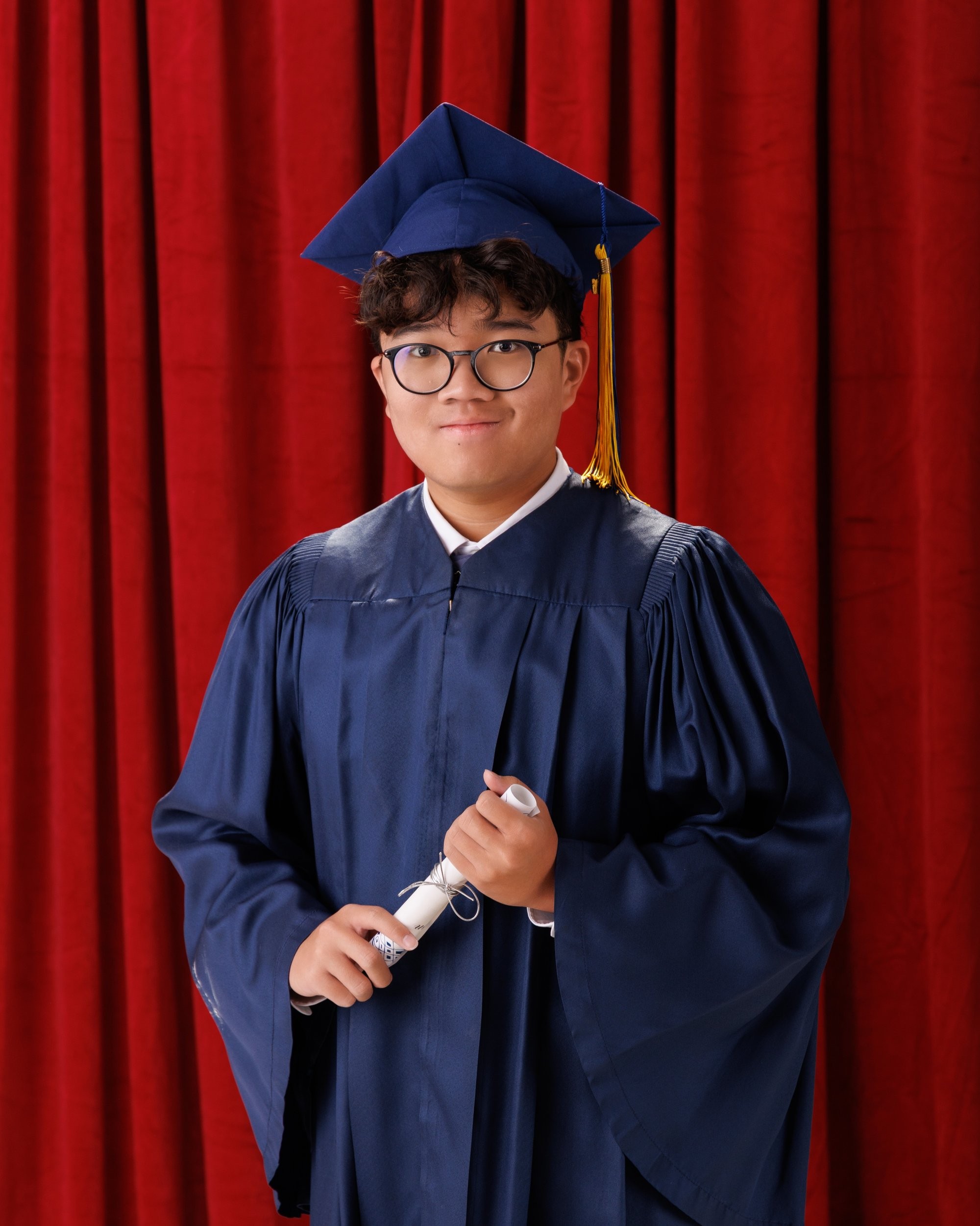 Graduating student holding diploma scroll in blue academic regalia, red theater background