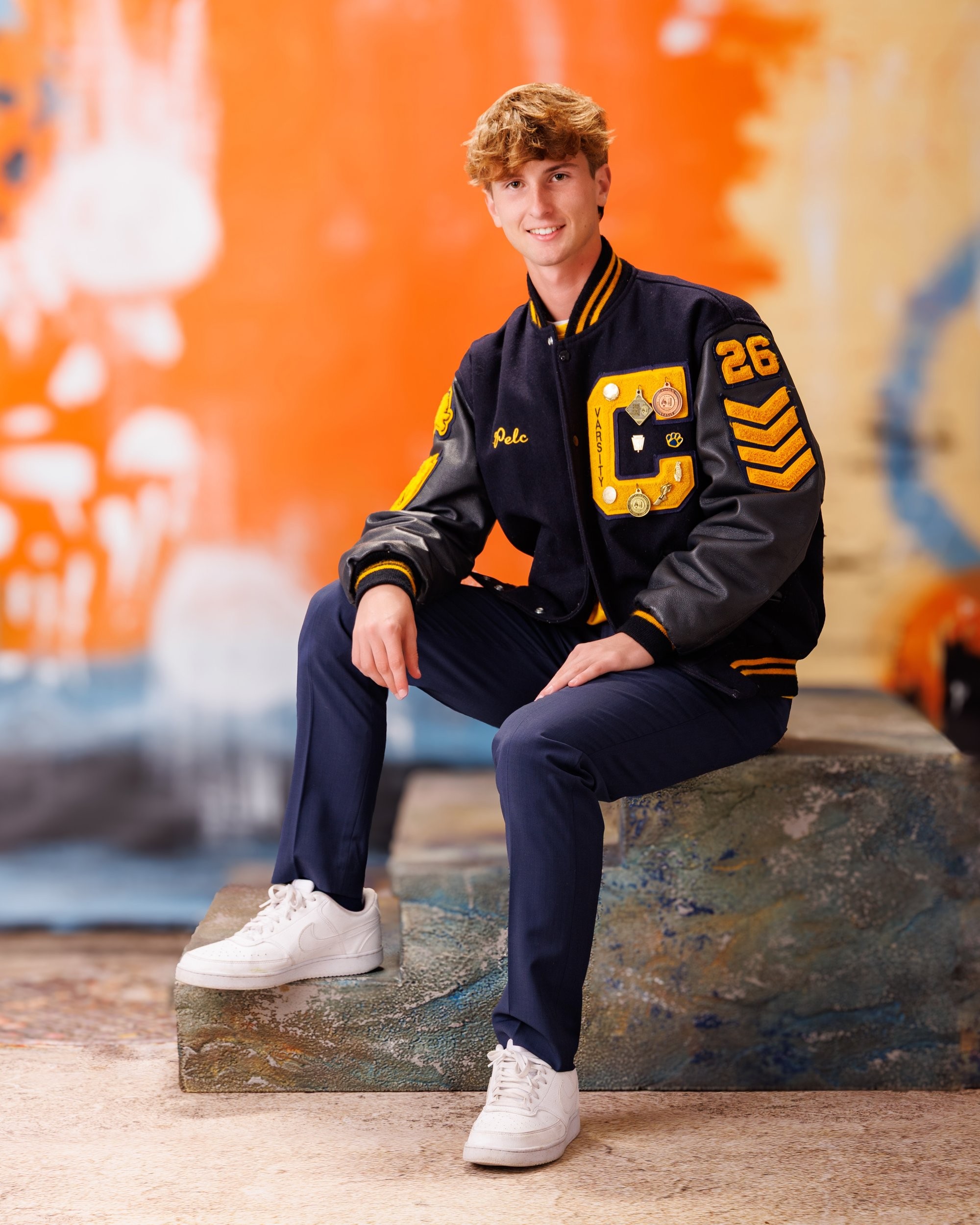 Cabrini High senior Brad balancing a Wilson basketball while seated on stone steps, wearing varsity attire and white sneakers.