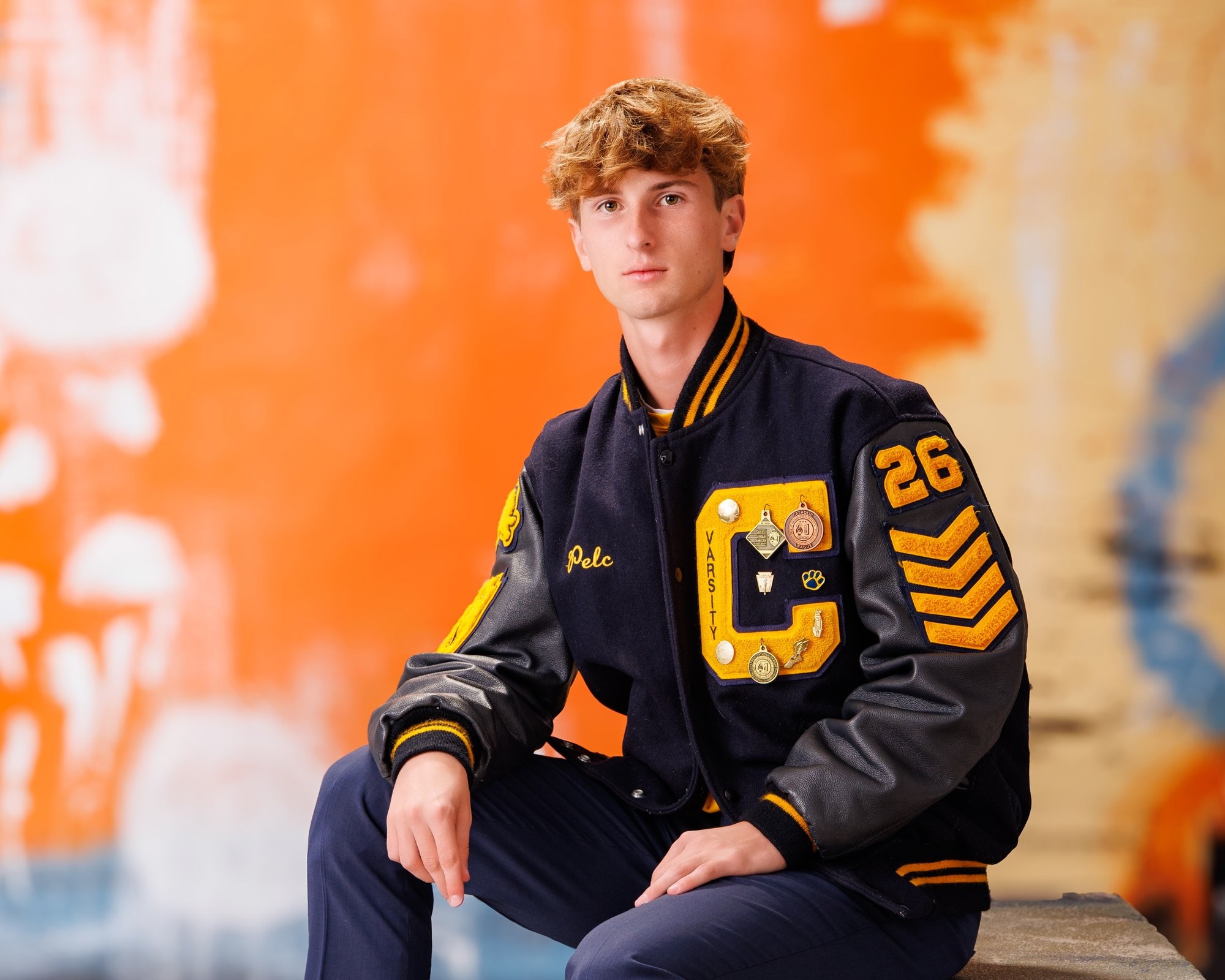 Cabrini High senior Brad posing with a varsity backpack featuring sports logos and 'Laborini' text, showcasing school spirit in a minimalist studio setting.