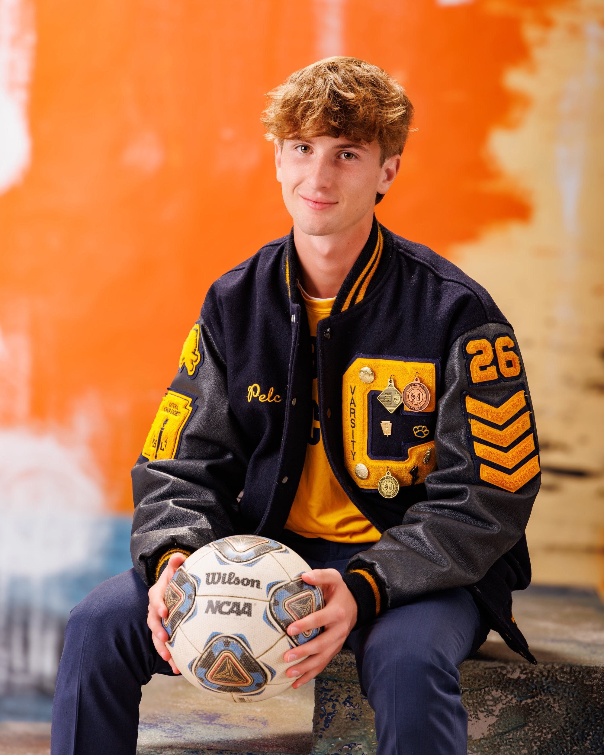 Cabrini High senior Brad posing with a varsity backpack featuring sports logos and 'Laborini' text, showcasing school spirit in a minimalist studio setting.