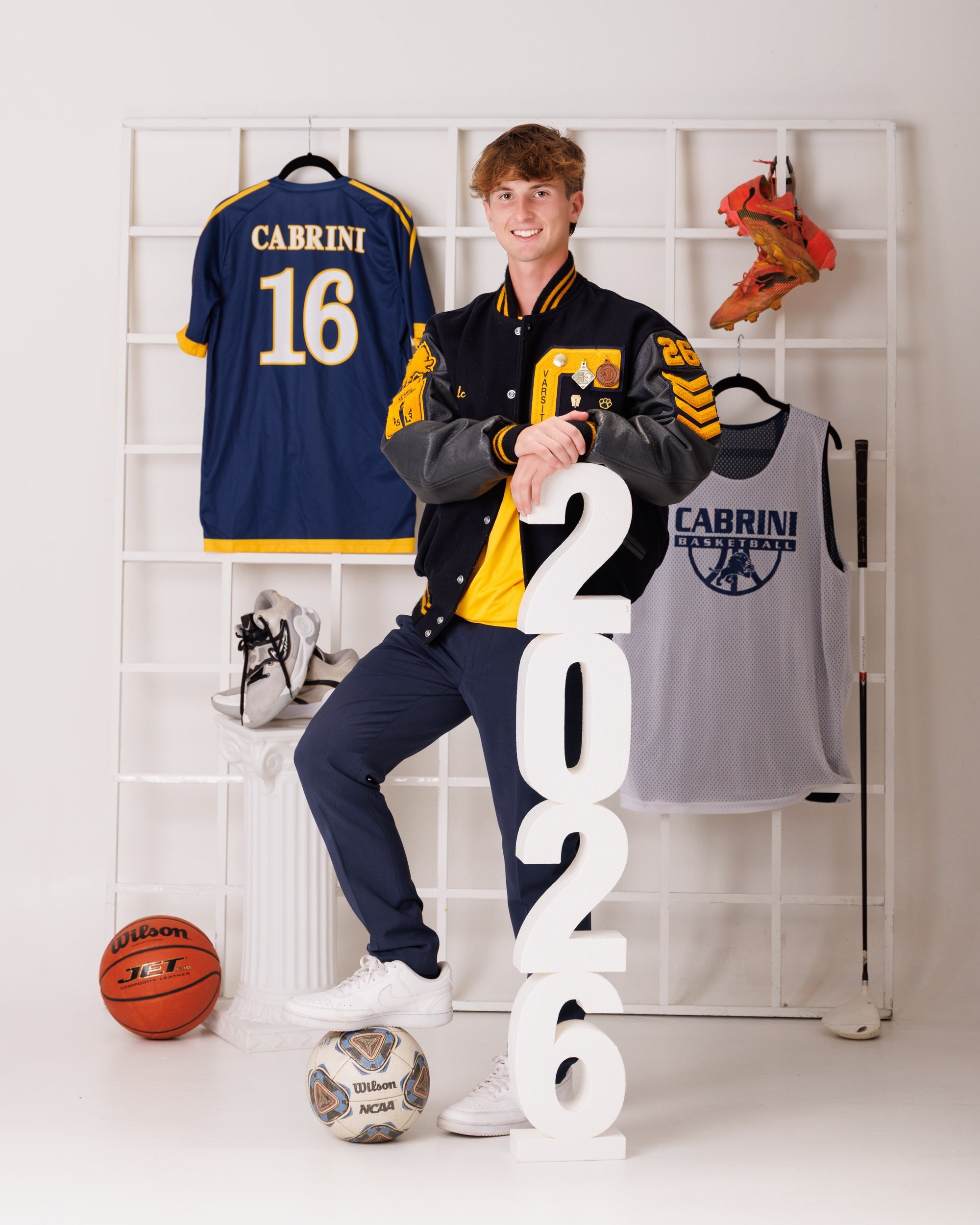 Cabrini High senior Brad posing with a varsity backpack featuring sports logos and 'Laborini' text, showcasing school spirit in a minimalist studio setting.