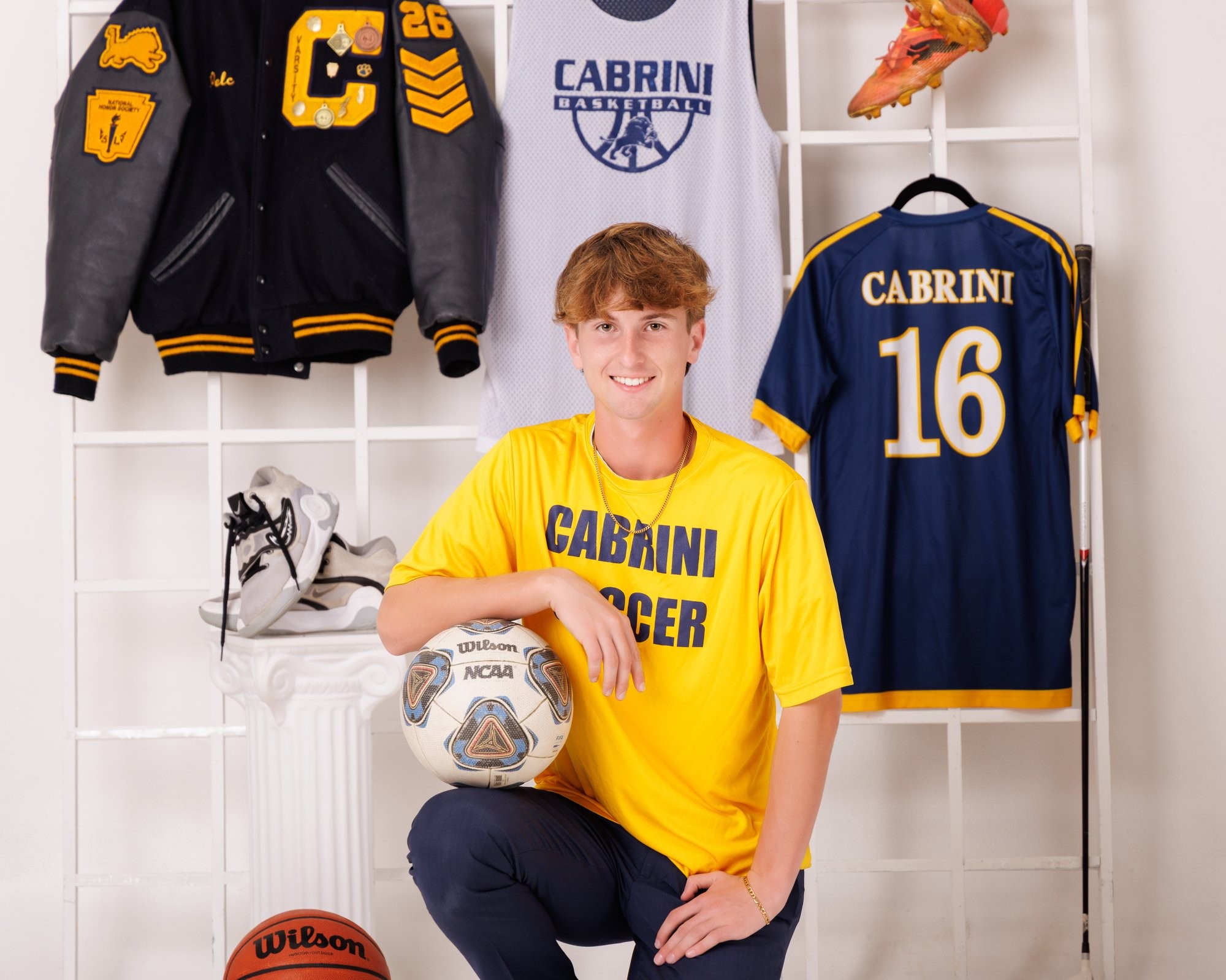 Cabrini High senior Brad posing with a varsity backpack featuring sports logos and 'Laborini' text, showcasing school spirit in a minimalist studio setting.