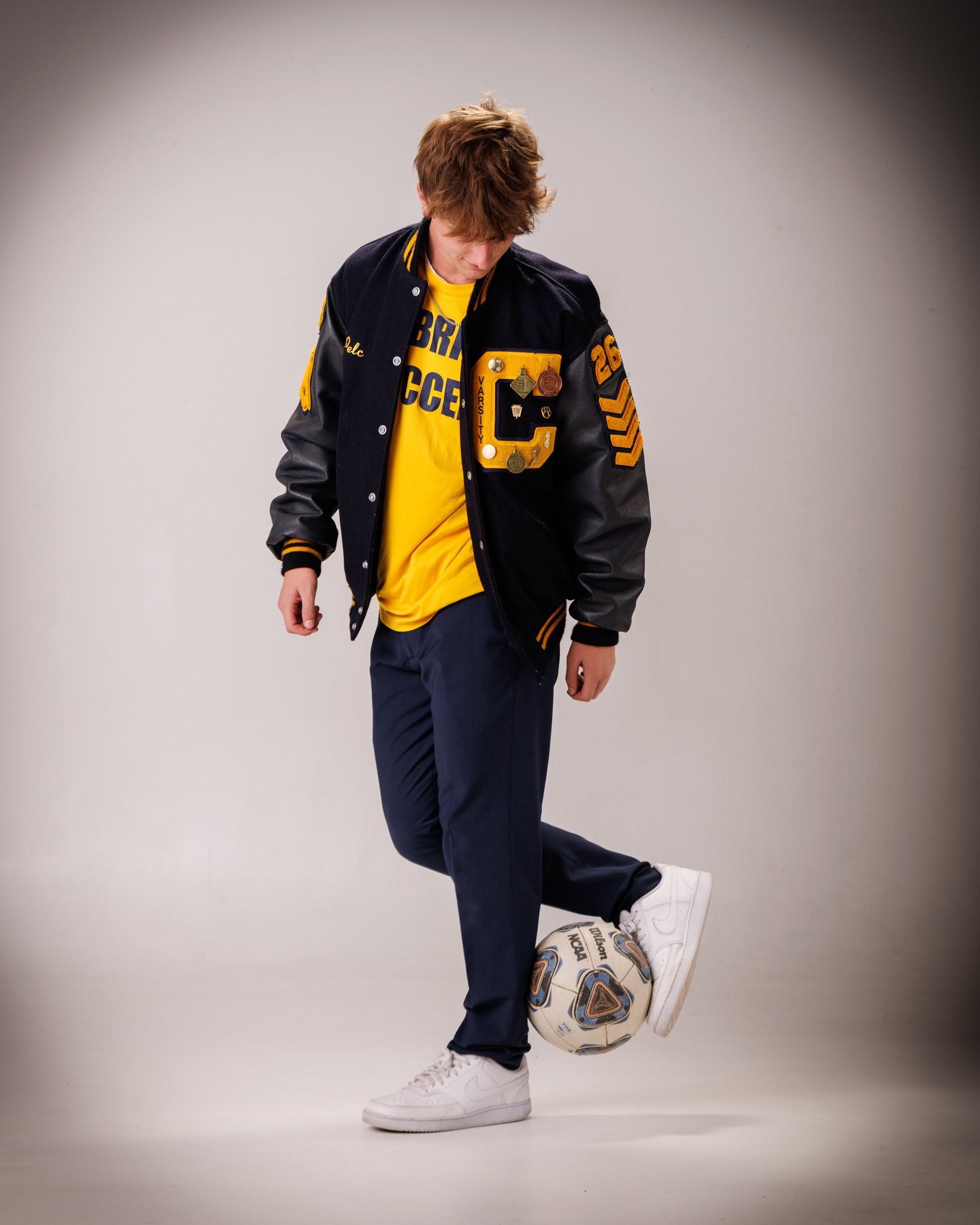 Cabrini High senior Brad posing with a varsity backpack featuring sports logos and 'Laborini' text, showcasing school spirit in a minimalist studio setting.