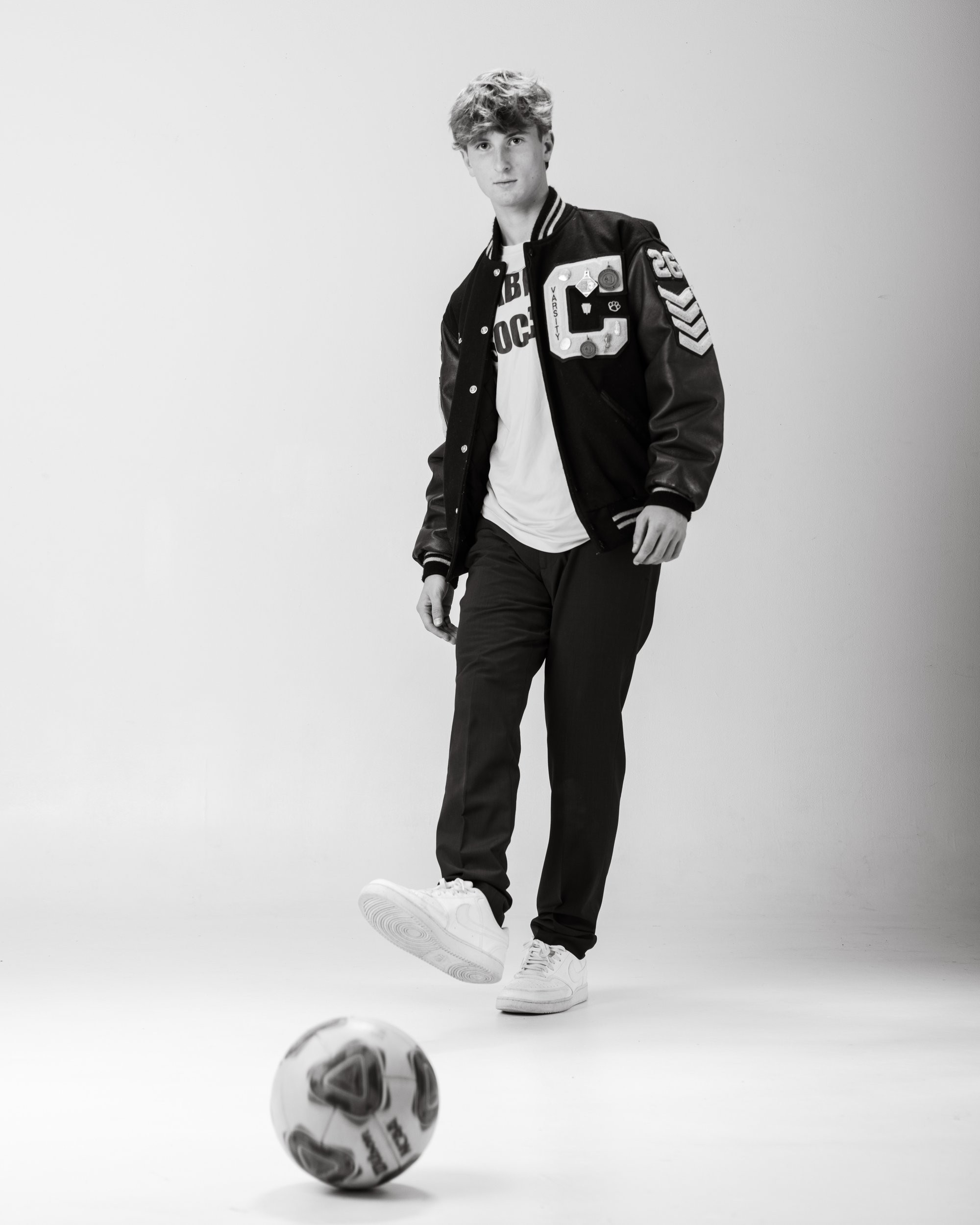 Cabrini High senior Brad posing with a varsity backpack featuring sports logos and 'Laborini' text, showcasing school spirit in a minimalist studio setting.