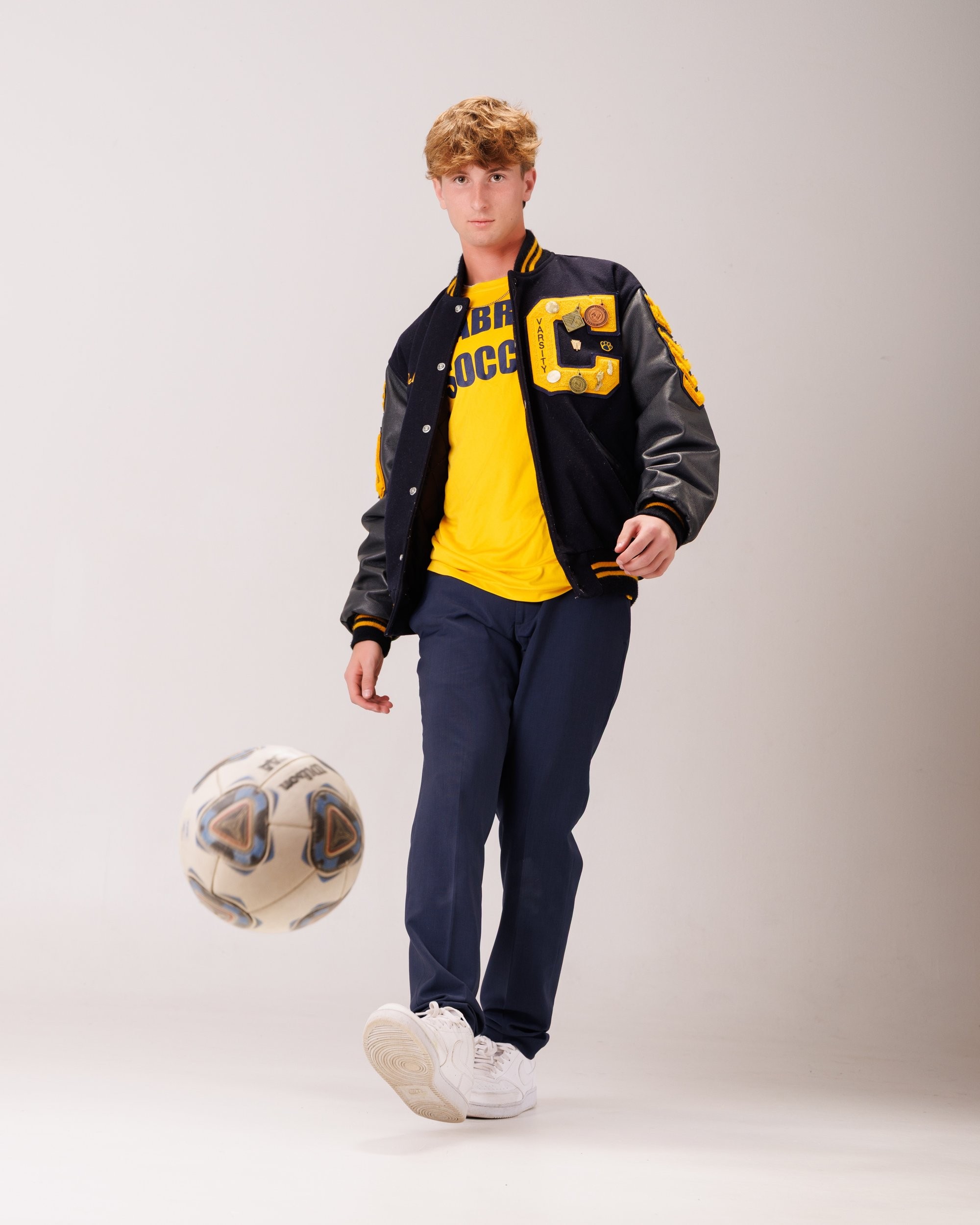 Cabrini High senior Brad posing with a varsity backpack featuring sports logos and 'Laborini' text, showcasing school spirit in a minimalist studio setting.