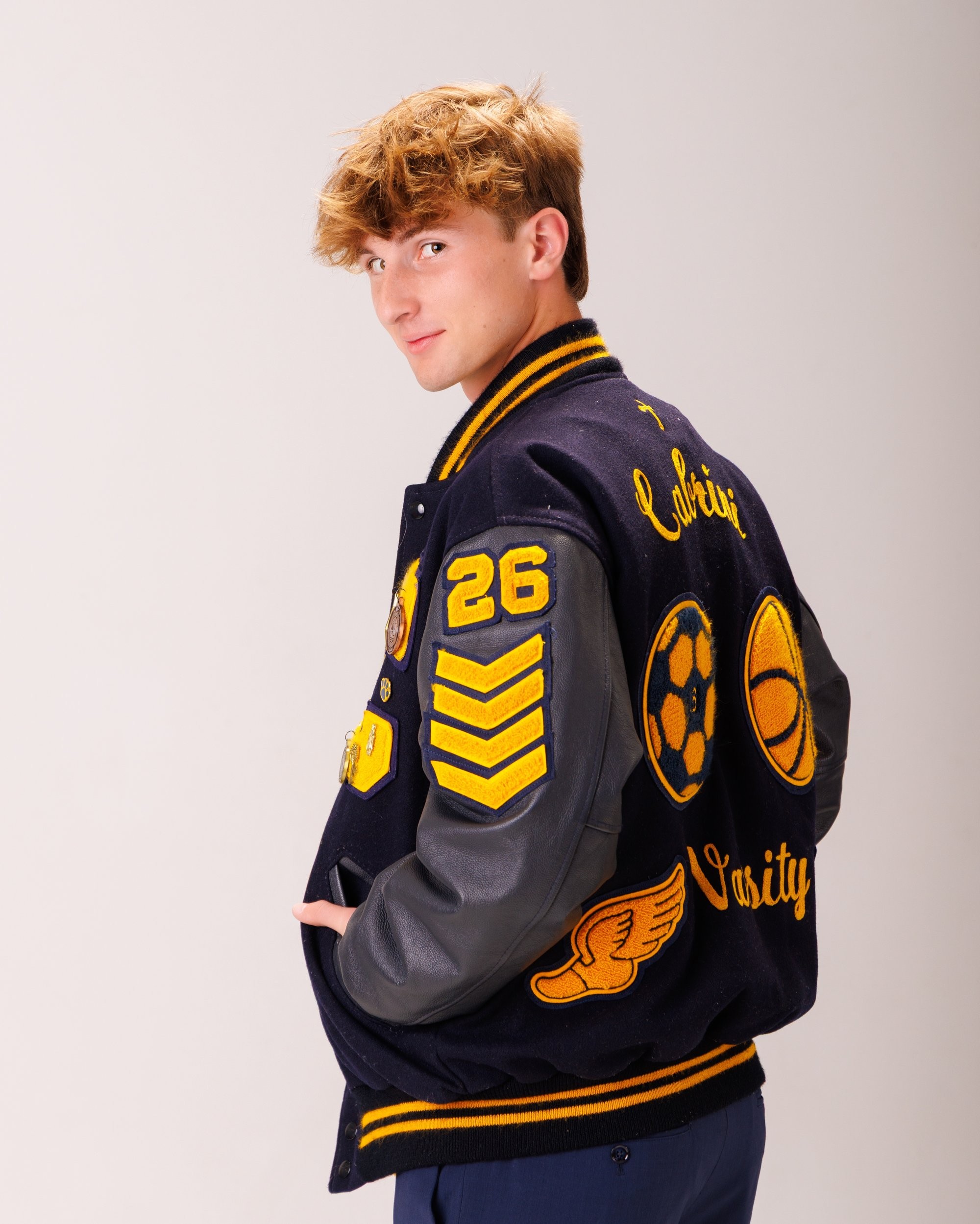 Cabrini High senior Brad posing with a varsity backpack featuring sports logos and 'Laborini' text, showcasing school spirit in a minimalist studio setting.